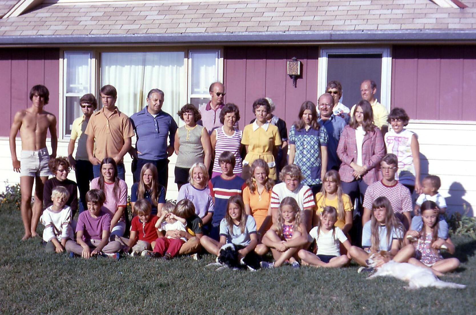 Large group of adults and children posing for a photo on the lawn in front of a purple house.