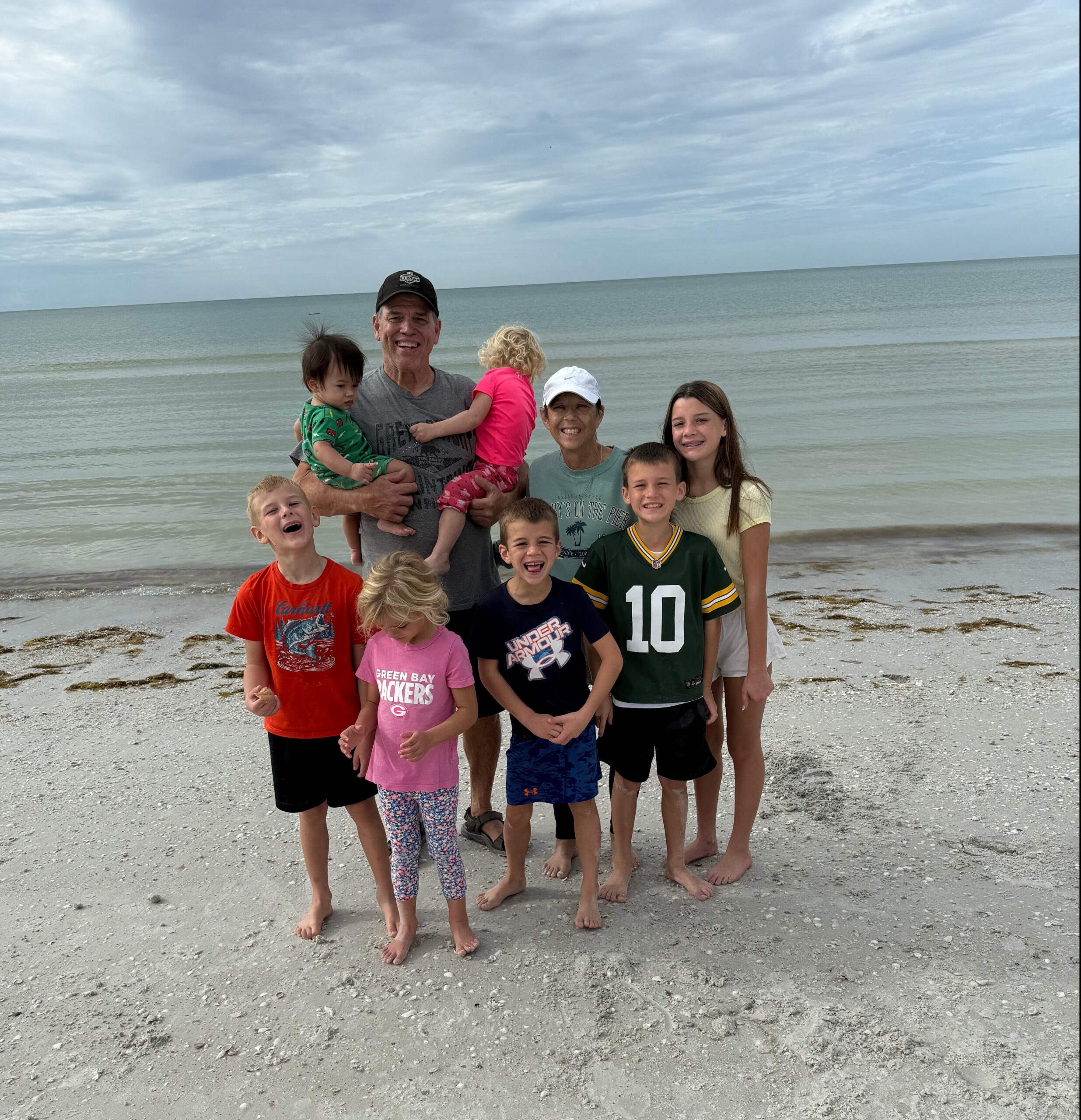 A large family group posing on a shell-strewn beach with the sea in the background, smiling at the camera.