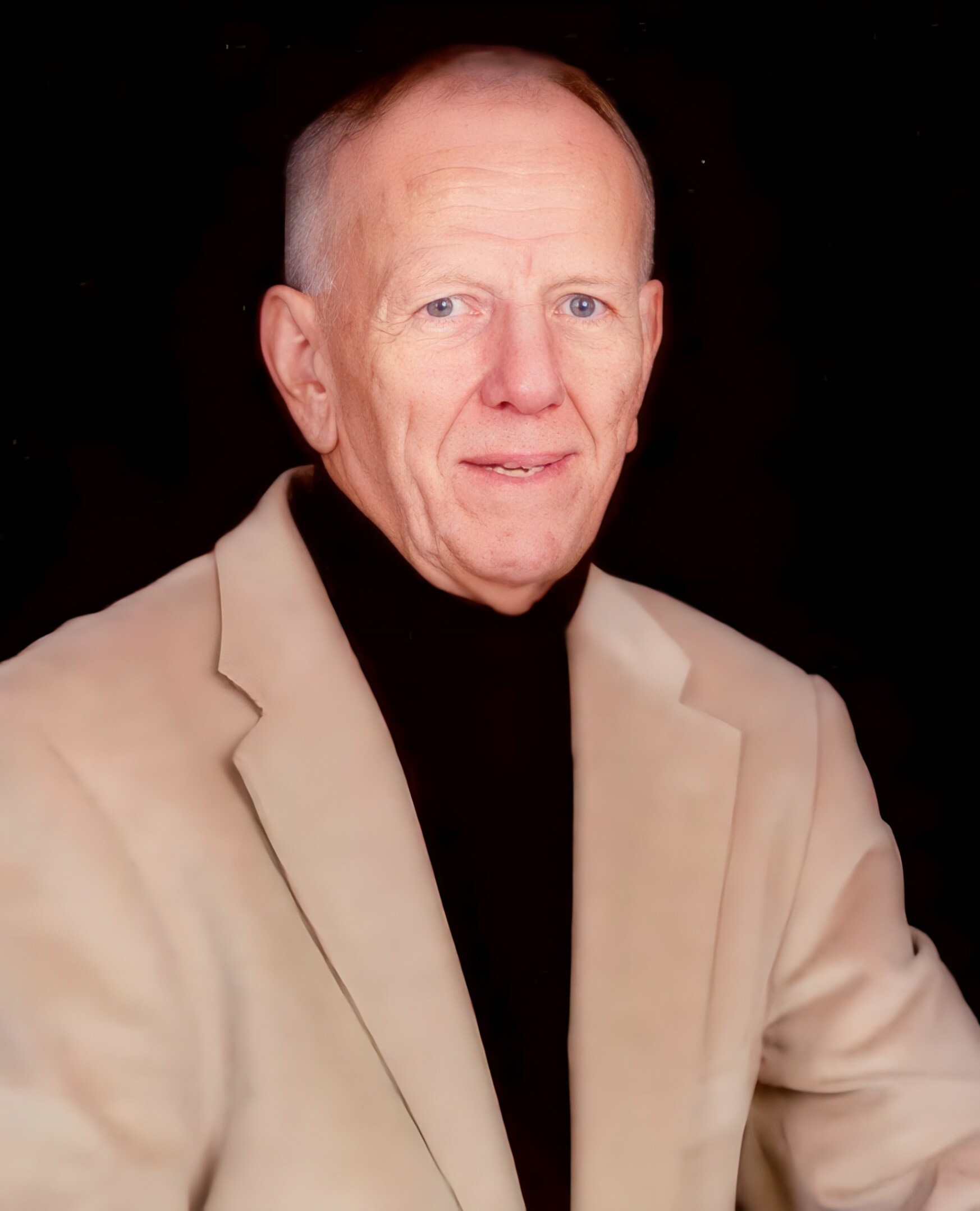 Close-up portrait of an older man with blue eyes, wearing a beige blazer over a black turtleneck, against a dark background, neutral expression.
