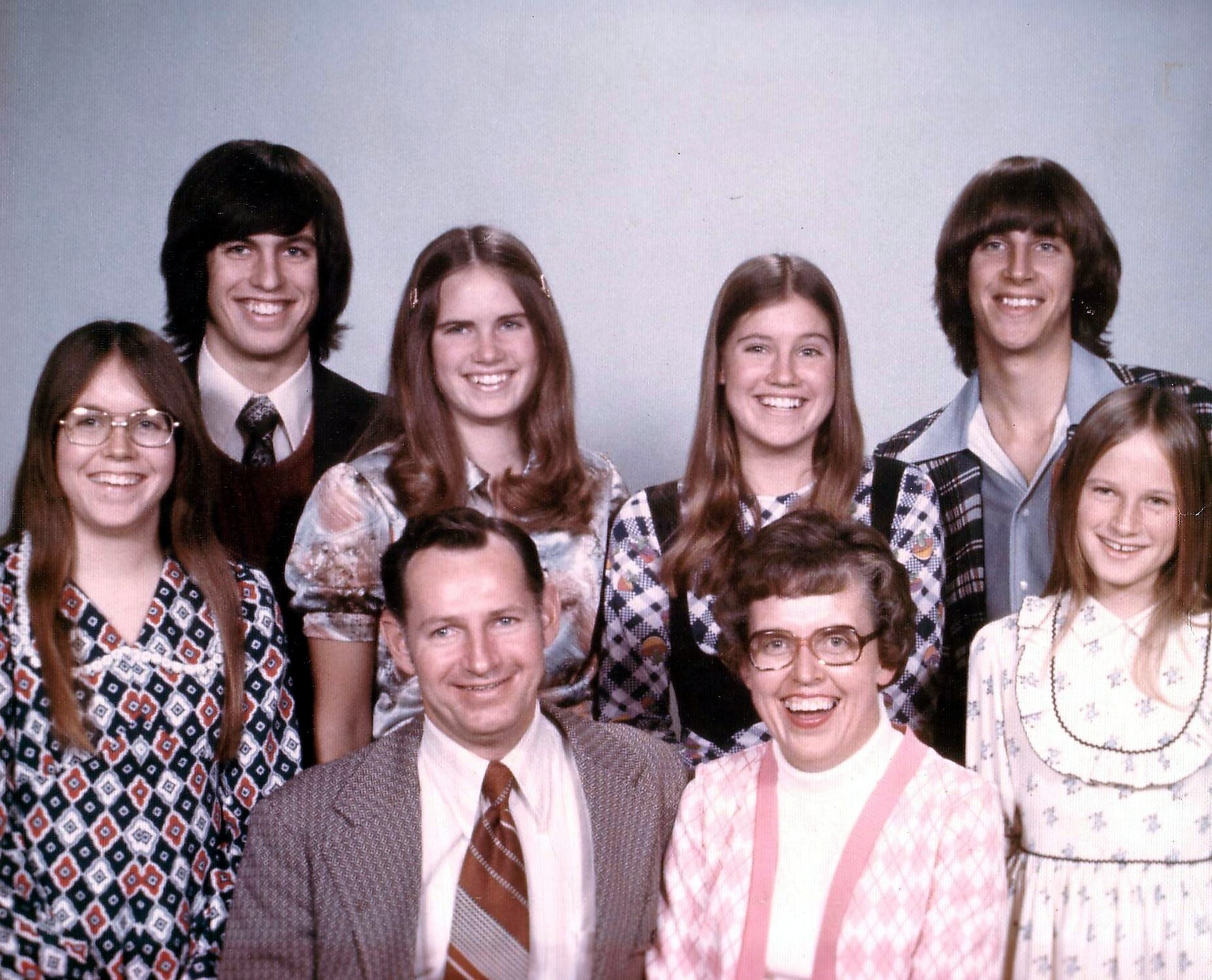 Group portrait of seven people in 1970s attire, smiling at the camera.