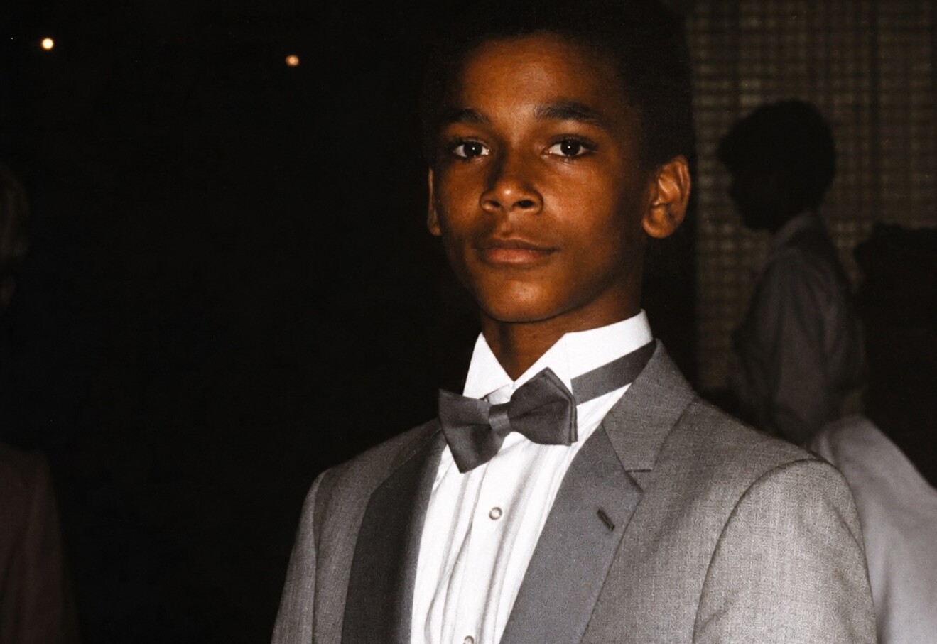 Young man in a light gray suit and dark bow tie at a nighttime formal event, looking at the camera.