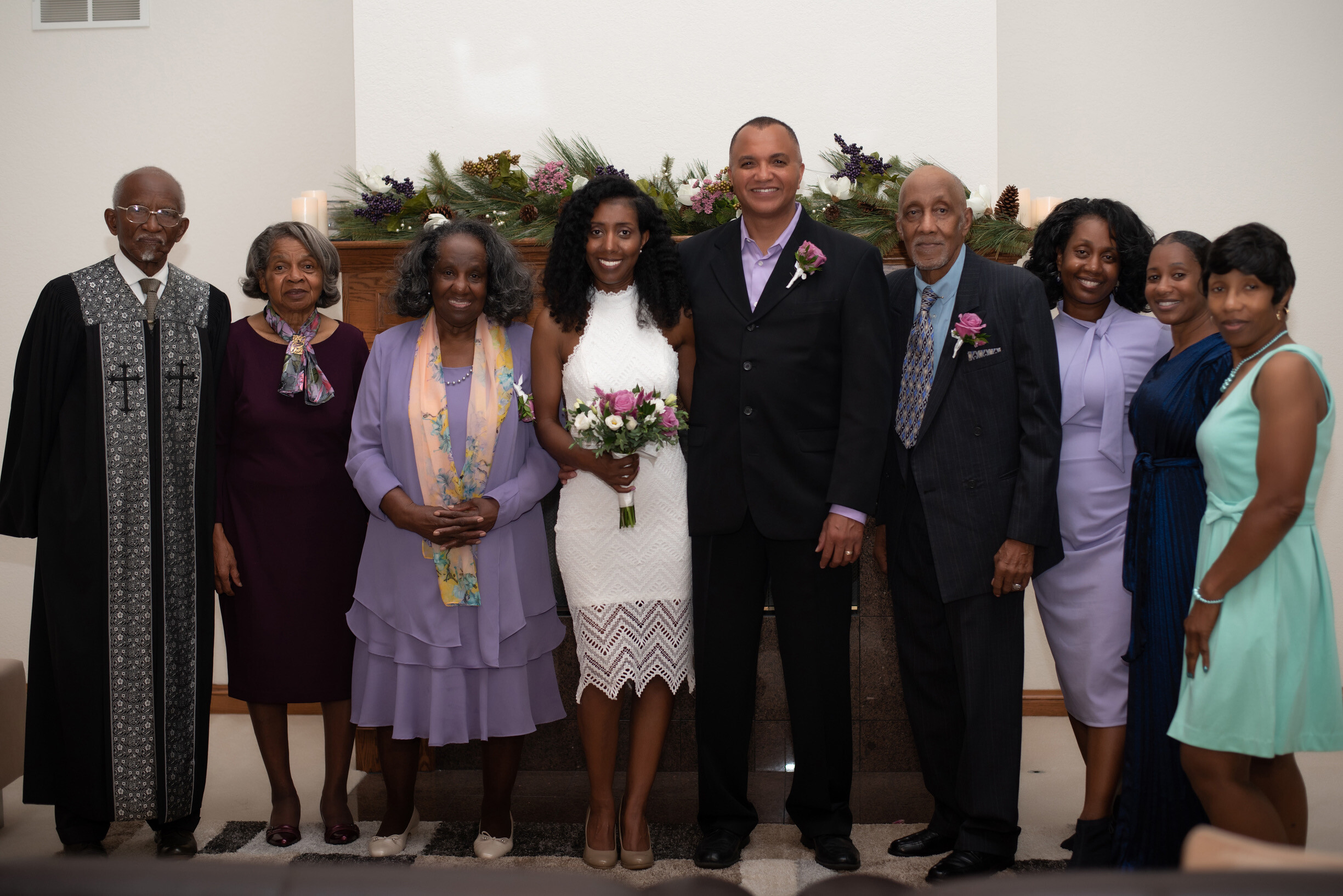 Group of nine adults dressed formally for a wedding, posing together on steps with the bride and groom at center, bouquet in hand and smiles all around.