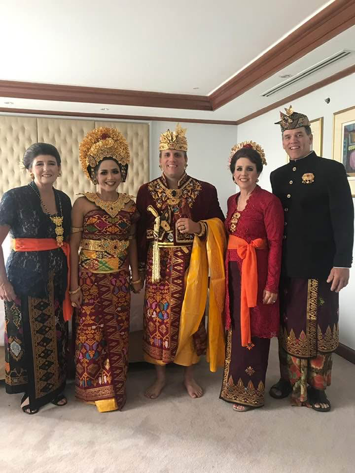Six people in ornate Balinese ceremonial outfits posing for a photo indoors.