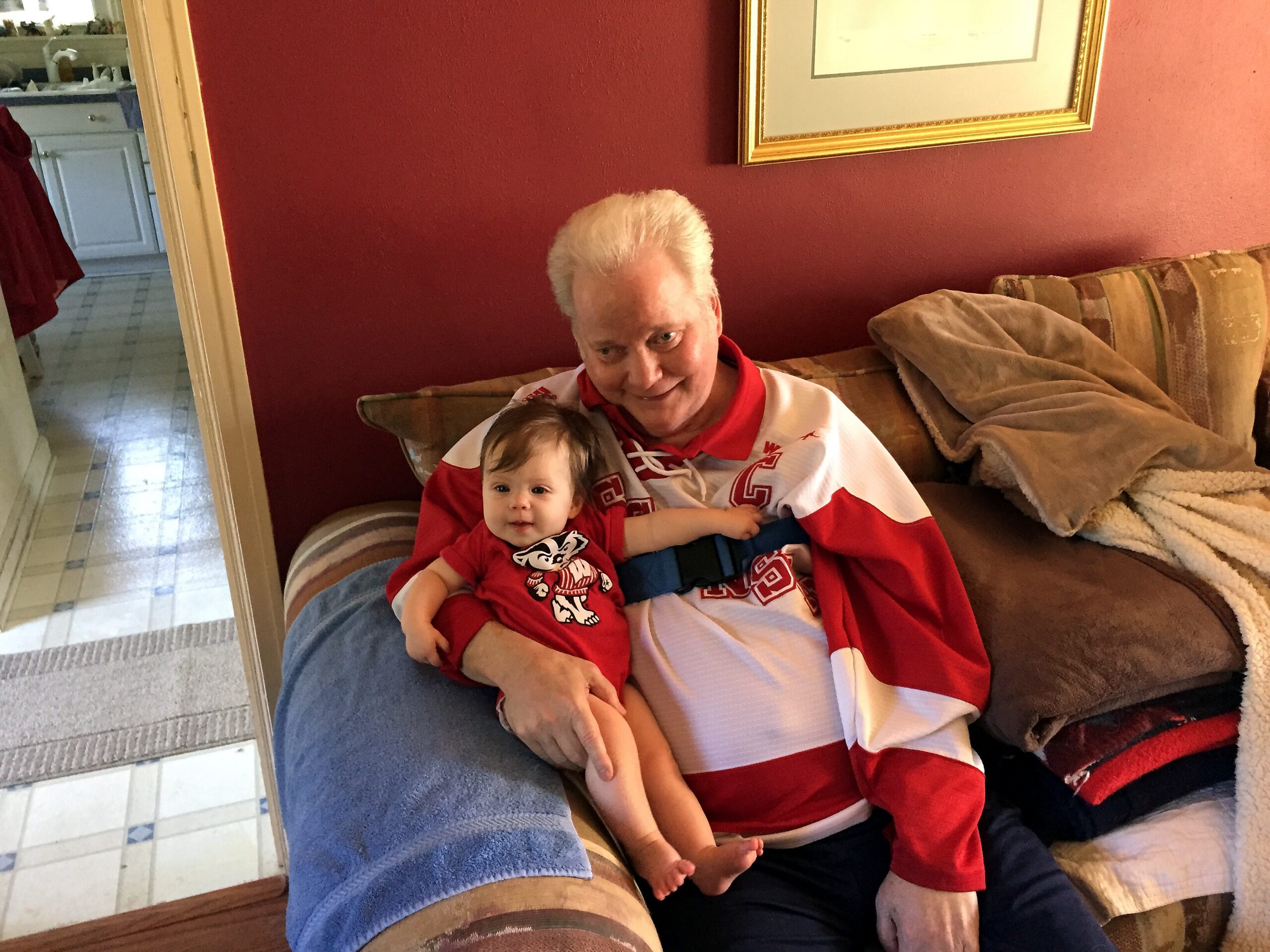 Older woman with white hair cuddling a baby on a striped sofa in a living room. (informative)