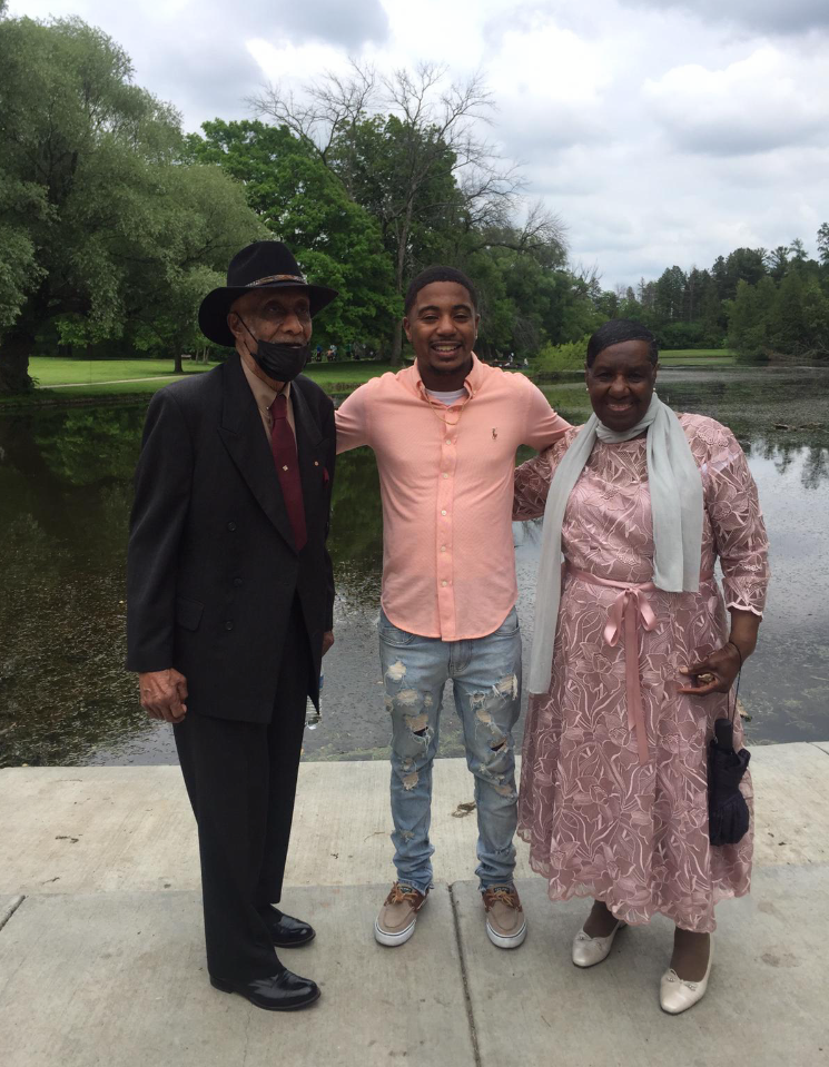 Three people posing together by a pond in a park, smiling at the camera.