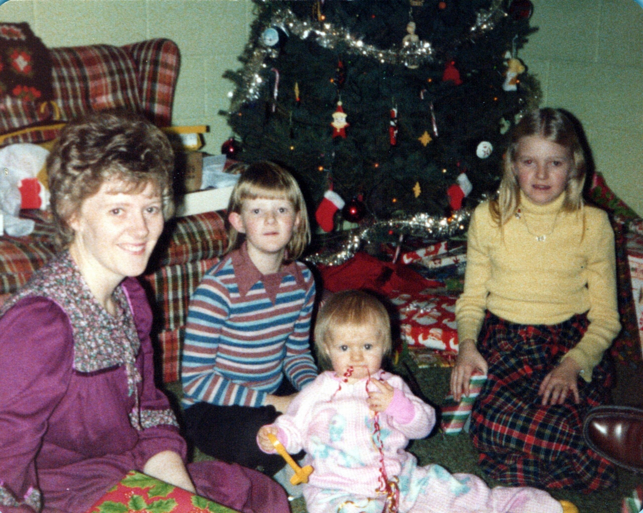 Family posing for a Christmas photo in a living room, gathered around a decorated tree with presents and stockings in the background.