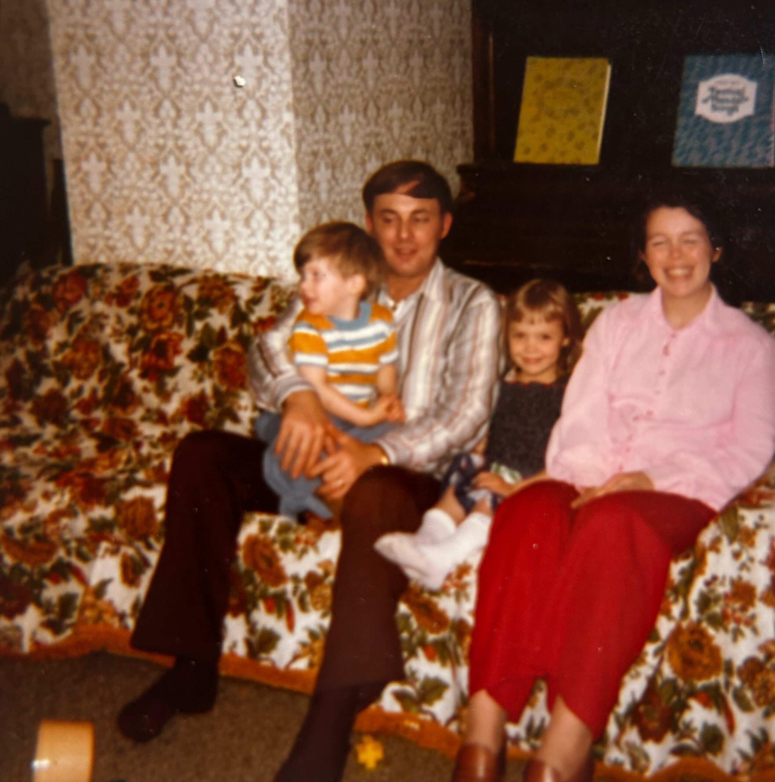 Group of family members posing for a photo on a floral sofa in a living room with patterned wallpaper.