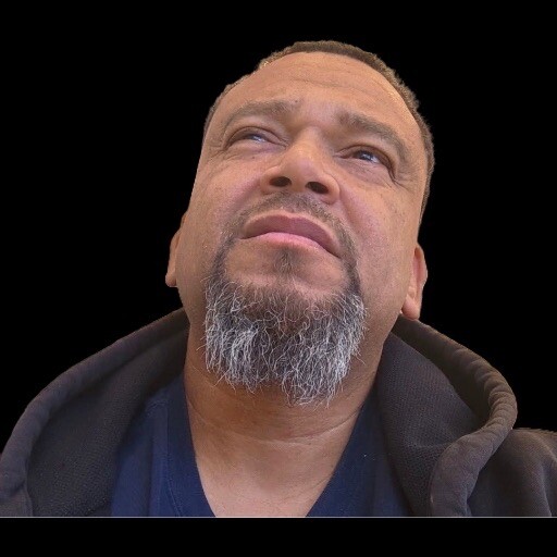 Close-up of a man with a gray beard looking upward against a black background.