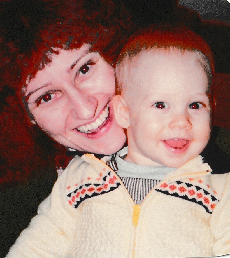 Mother with red hair smiling and cuddling a happy baby in a light sweater beside her.