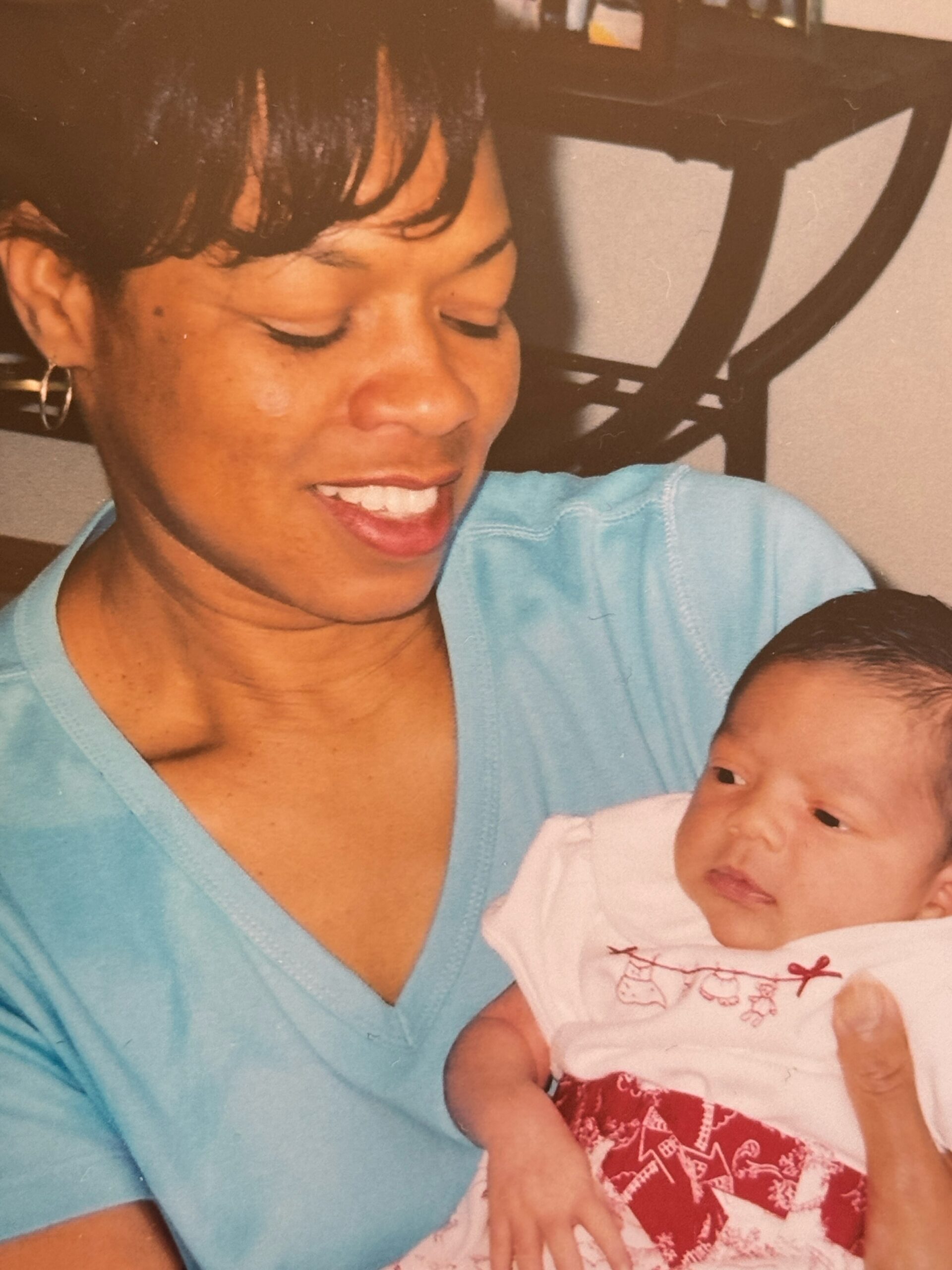 Woman smiles with eyes closed while holding a baby in her arms indoors.
