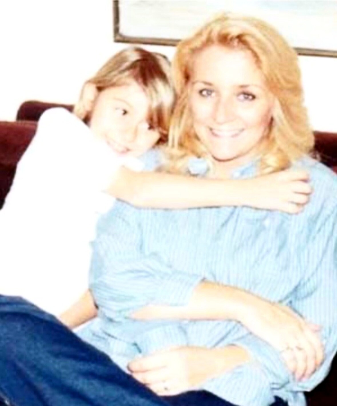 Smiling blonde woman on a couch with a young girl hugging her from the side.