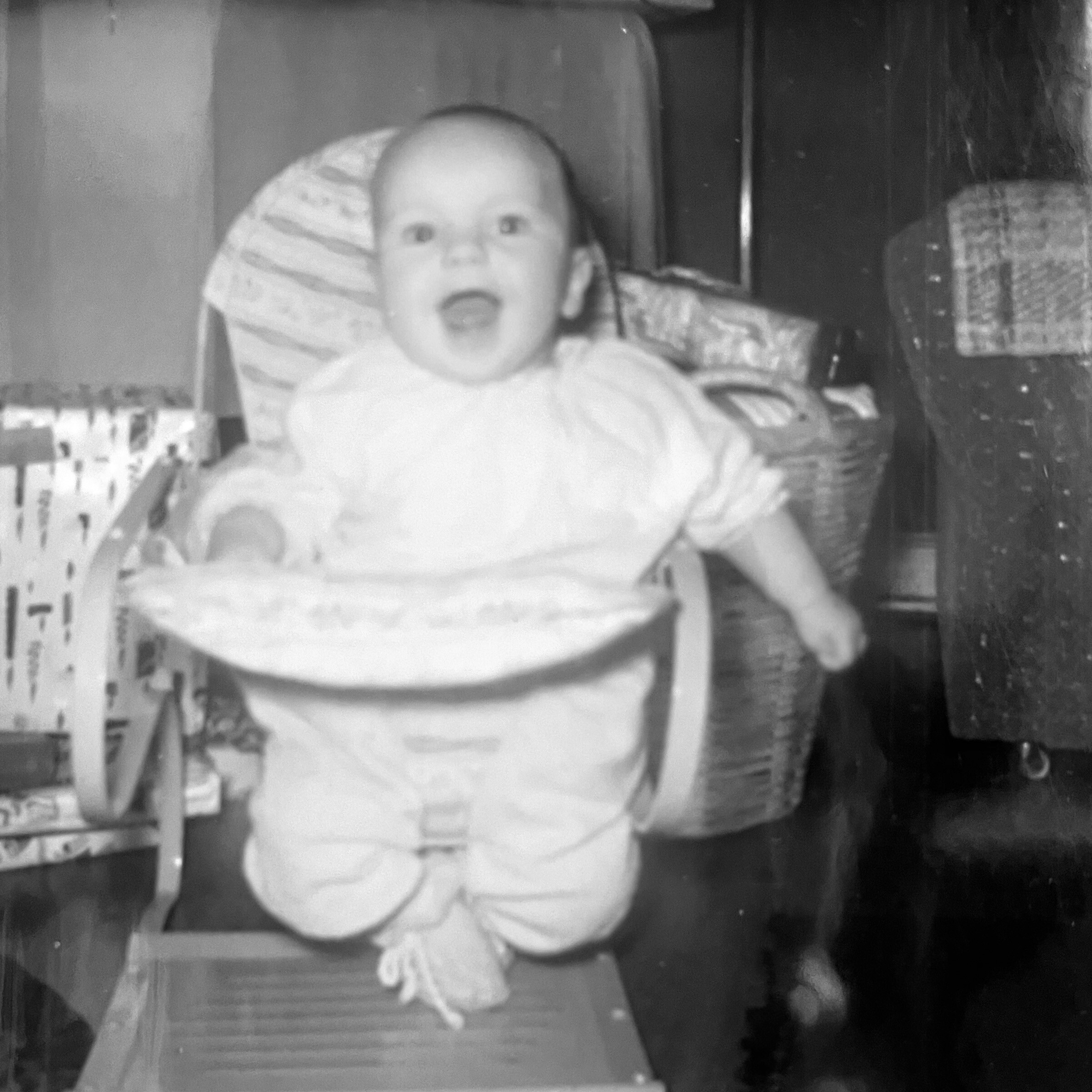 Infant secured in a car seat wearing a light-colored outfit with harnesses visible.