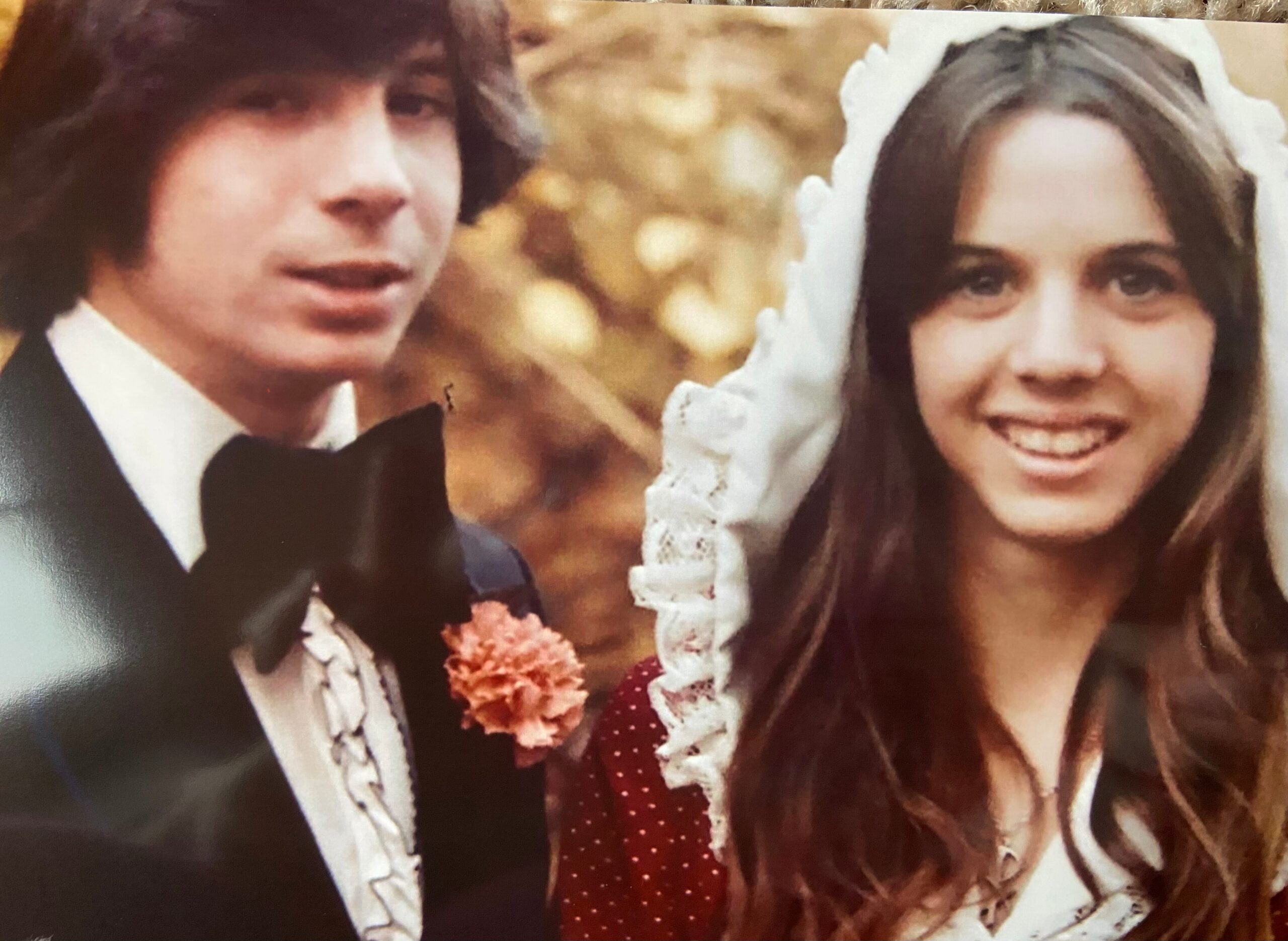 Close-up of a smiling bride and groom in wedding attire, the groom in a tuxedo with a bow tie and the bride wearing a veil.