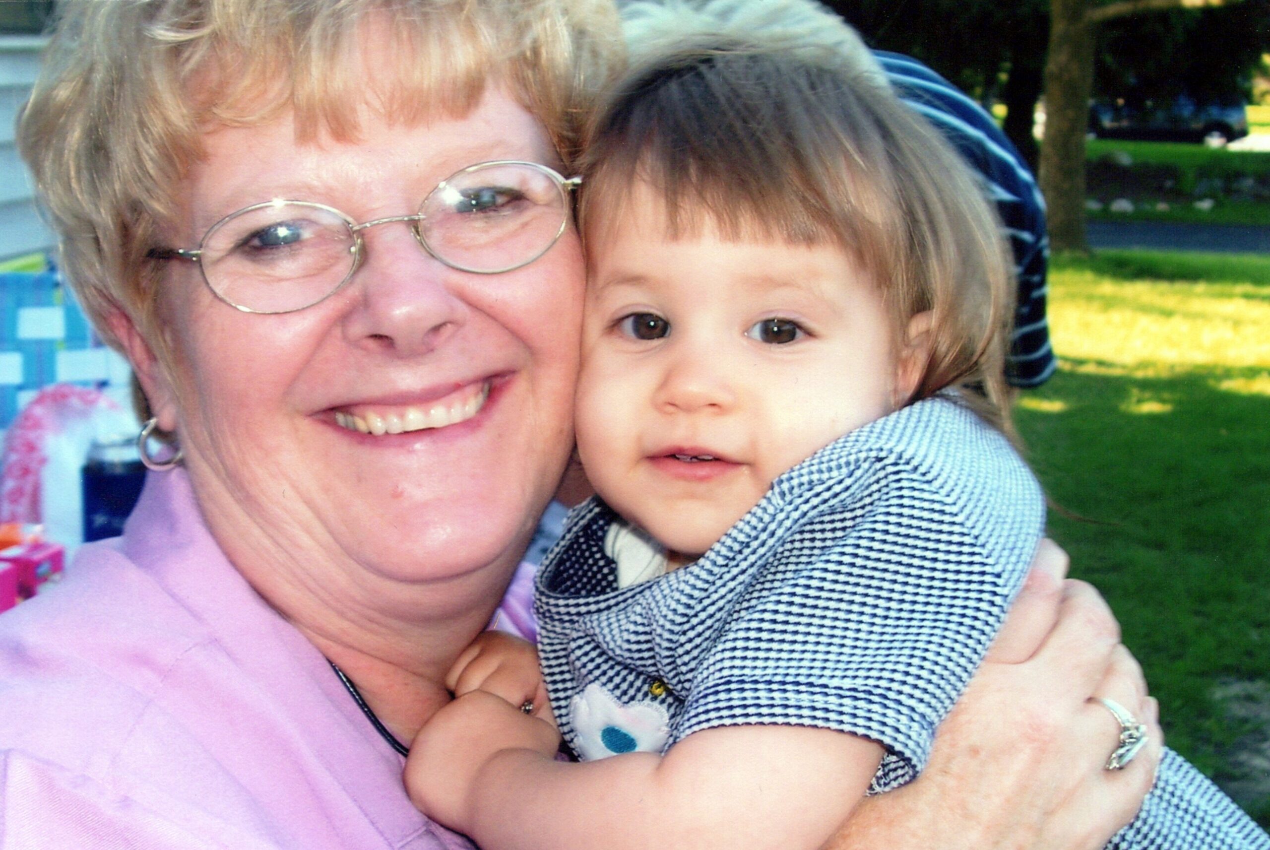 Smiling grandmother holding a young child outdoors in a close embrace.
