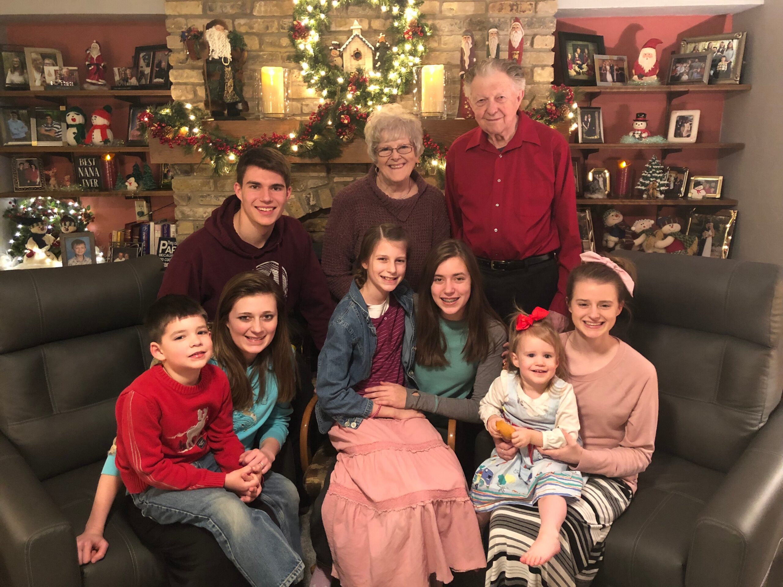 A family group posing on a sofa in a Christmas-decorated living room with a lit Christmas tree and photos on the shelves behind them.