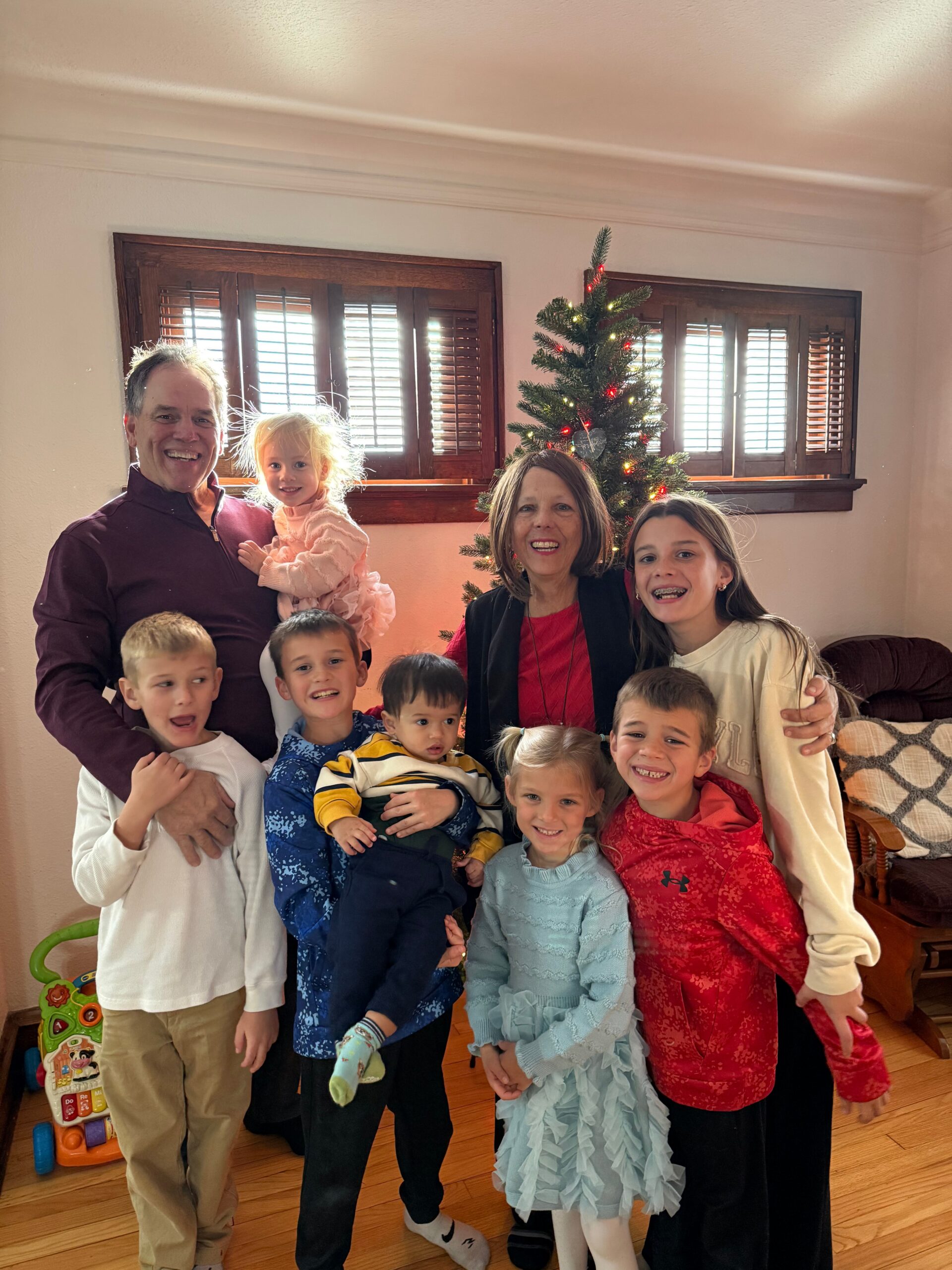 Smiling family posing indoors beside a lit Christmas tree in a living room.