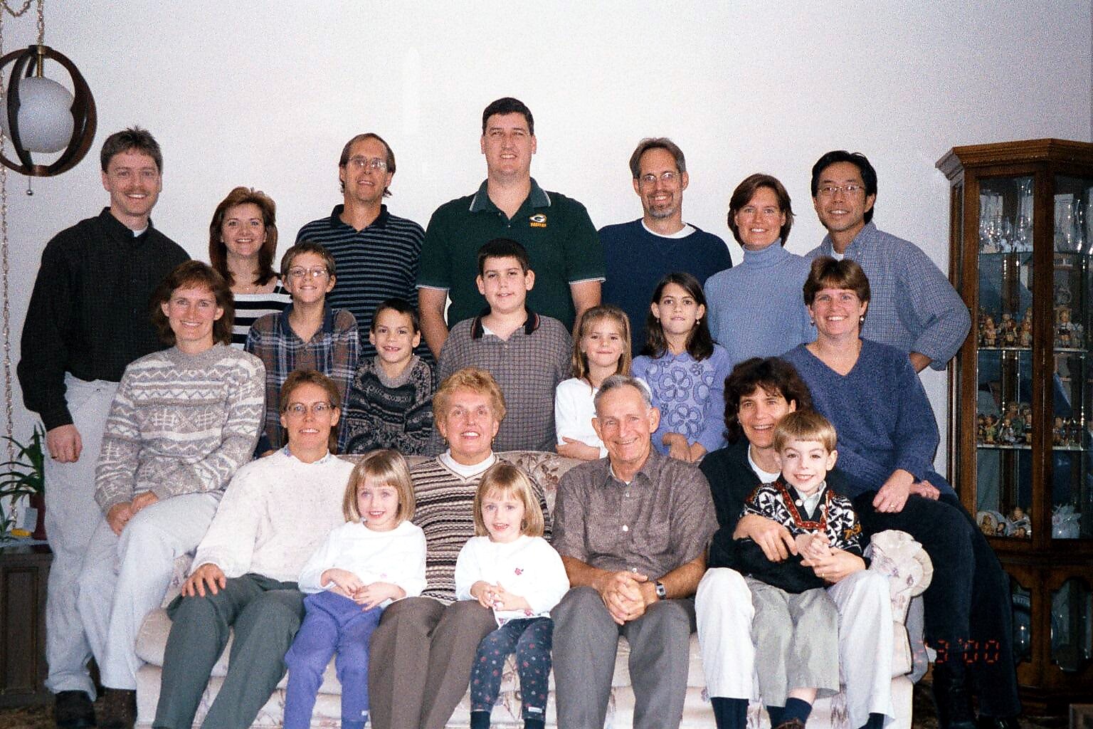 A large multi-generational family poses together in a living room for a group photo on a sofa and chairs.