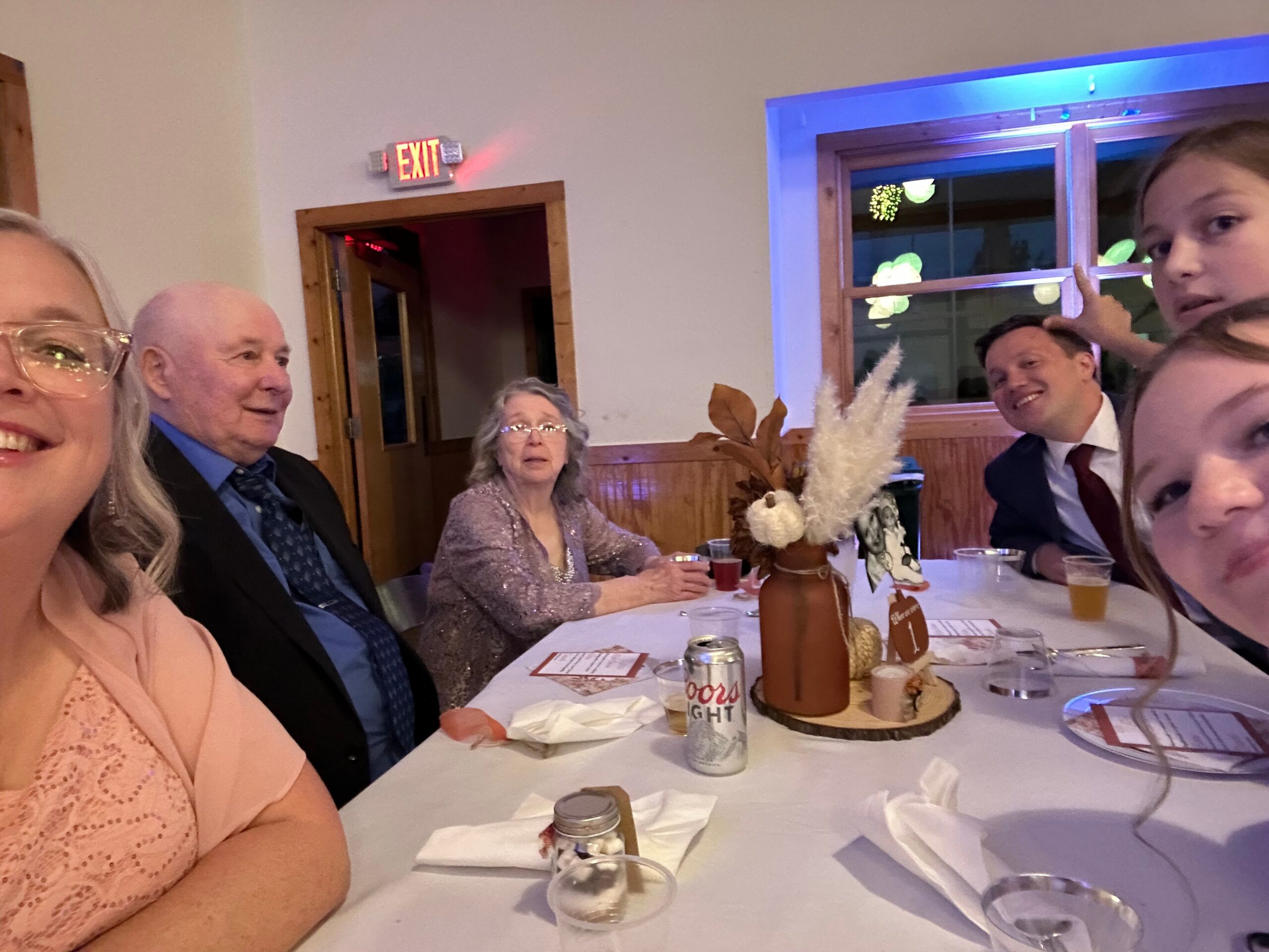 Group of adults seated around a table at a indoor celebration, with drinks and festive decorations on the table.