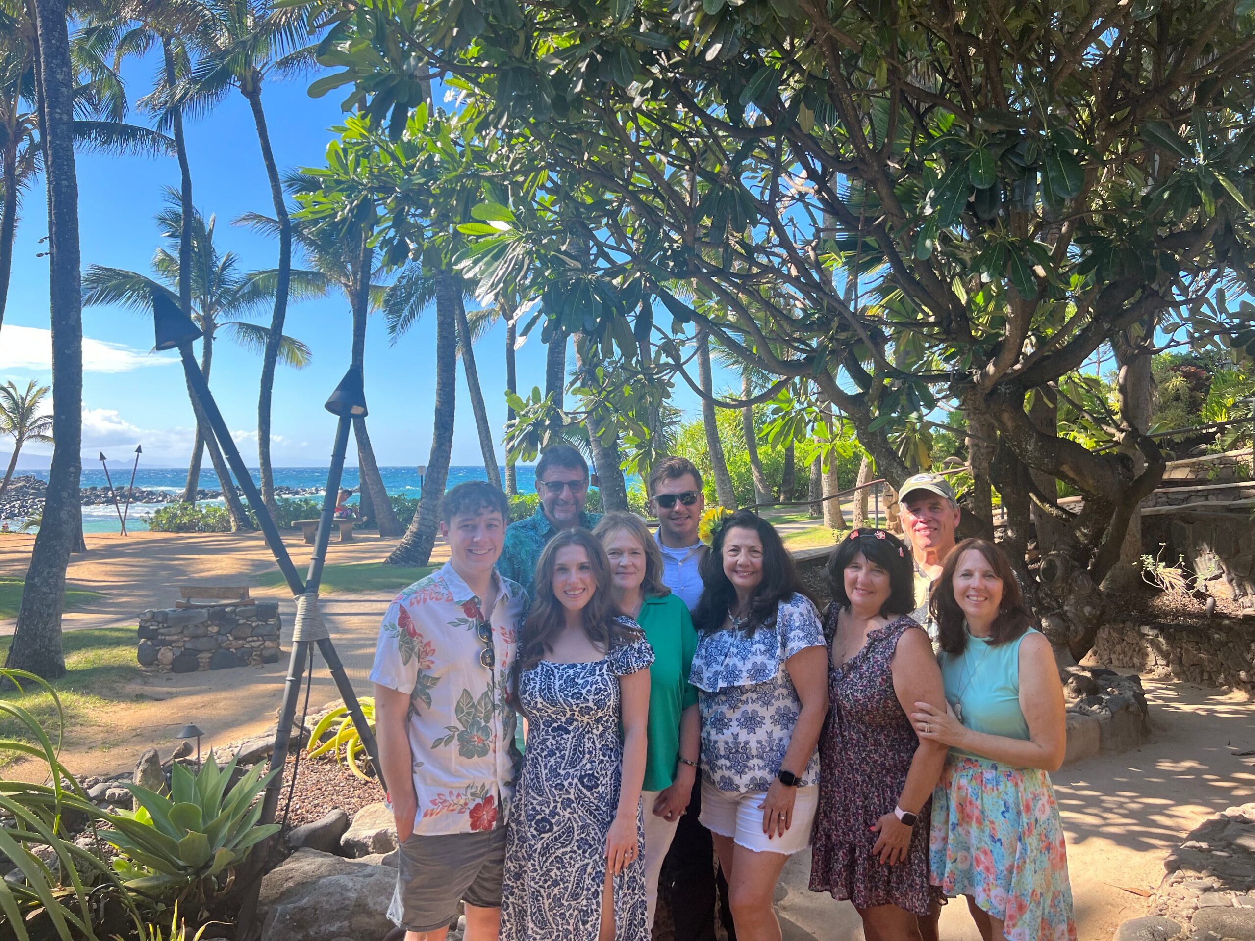 Group of smiling people posing for a photo on a sunny tropical beach with palm trees in the background.