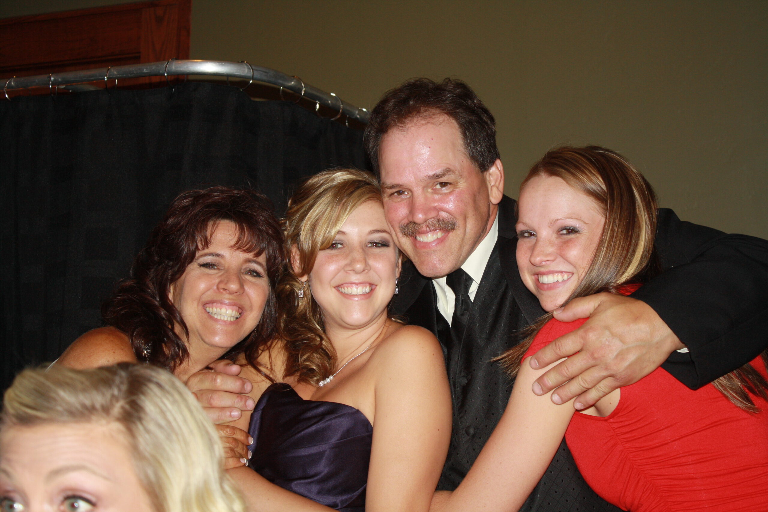 Group of five adults in formal wear smiling and hugging for a photo at a party.