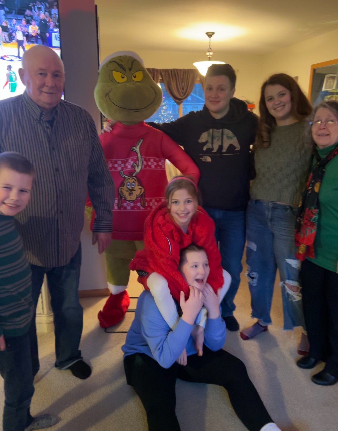 Group of family members posing with a Grinch mascot indoors during a holiday gathering.