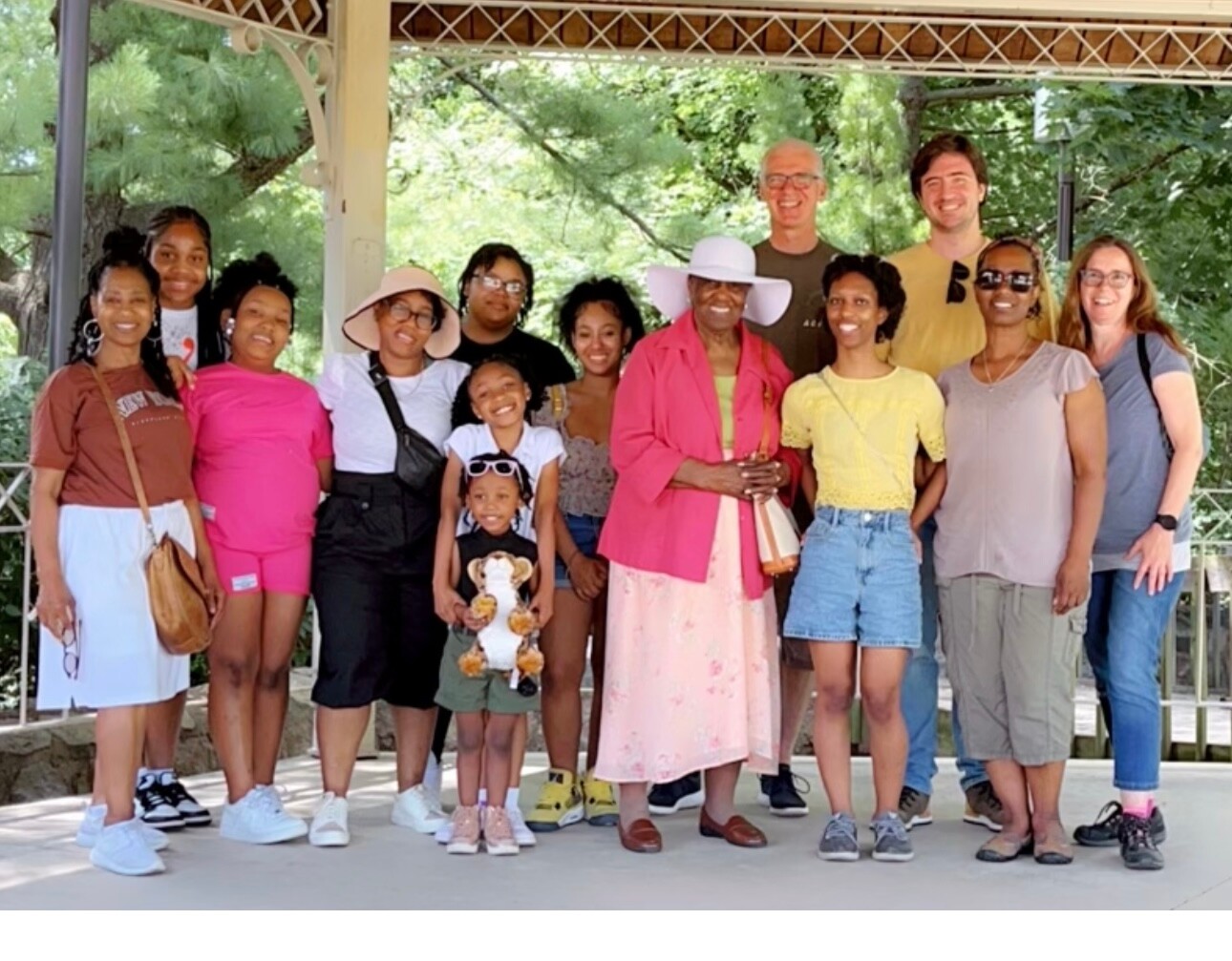 Diverse group of adults and children posing outdoors under a pavilion, smiling for a group photo.