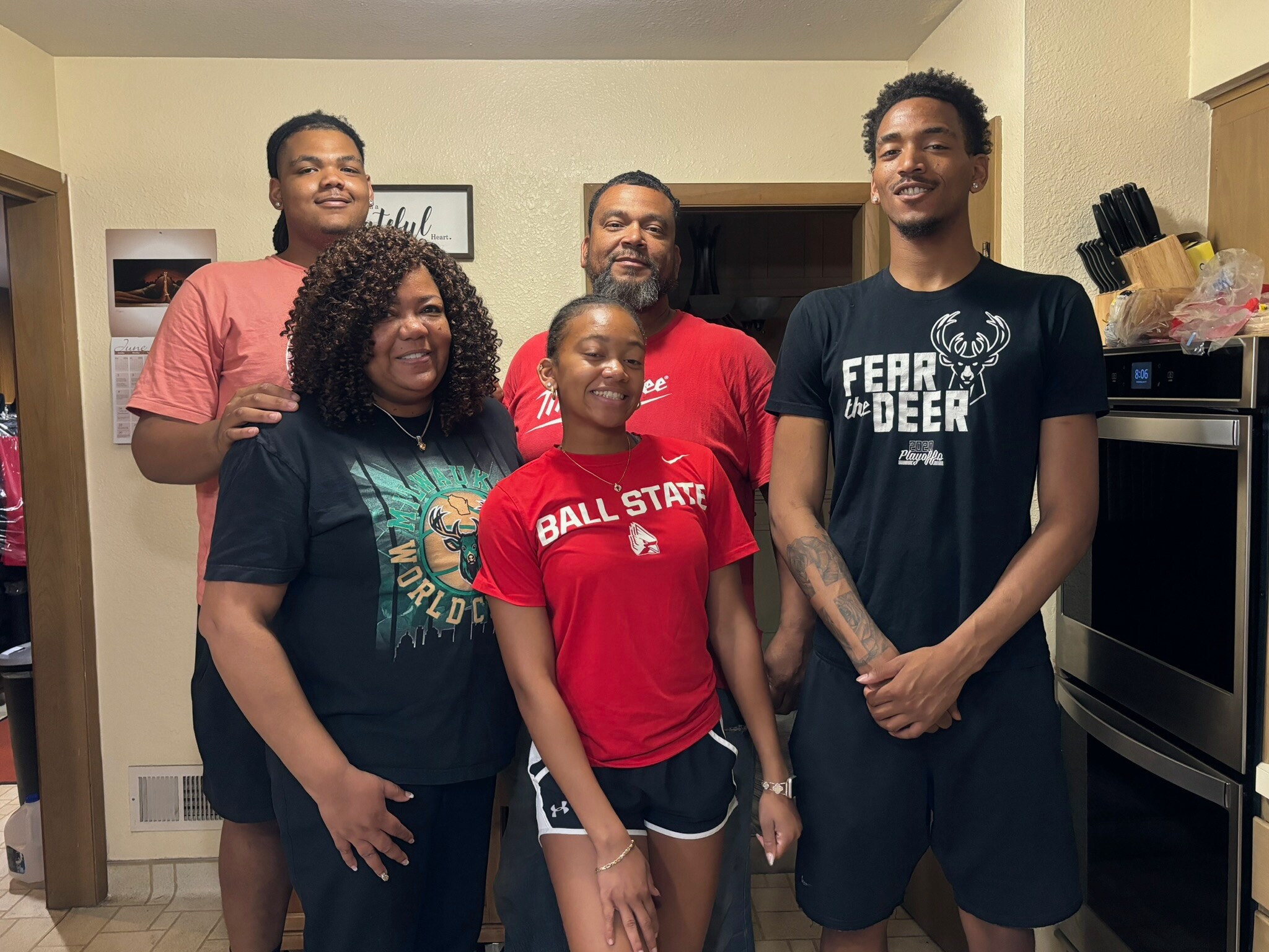 Five people posing together in a kitchen, all smiling at the camera.