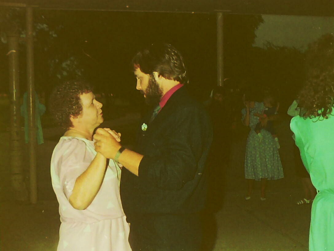 Couple dancing closely at night, holding hands and gazing at each other at a social gathering.