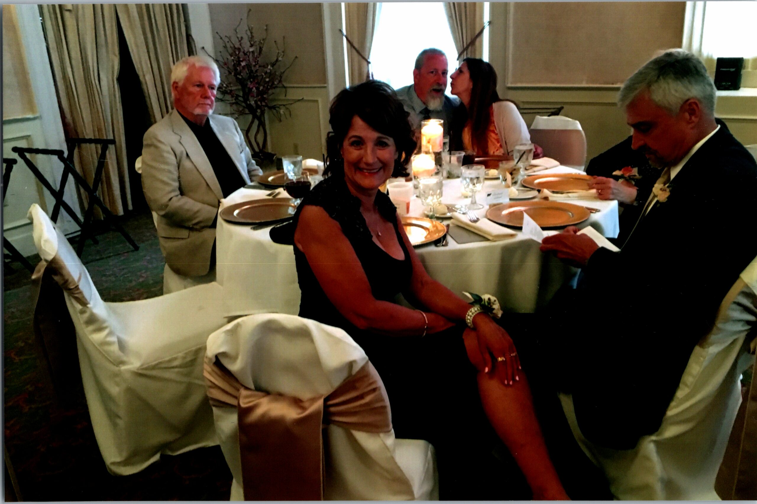 Group of adults seated around a candlelit banquet table at a formal dinner, one woman smiling at the camera in the foreground.