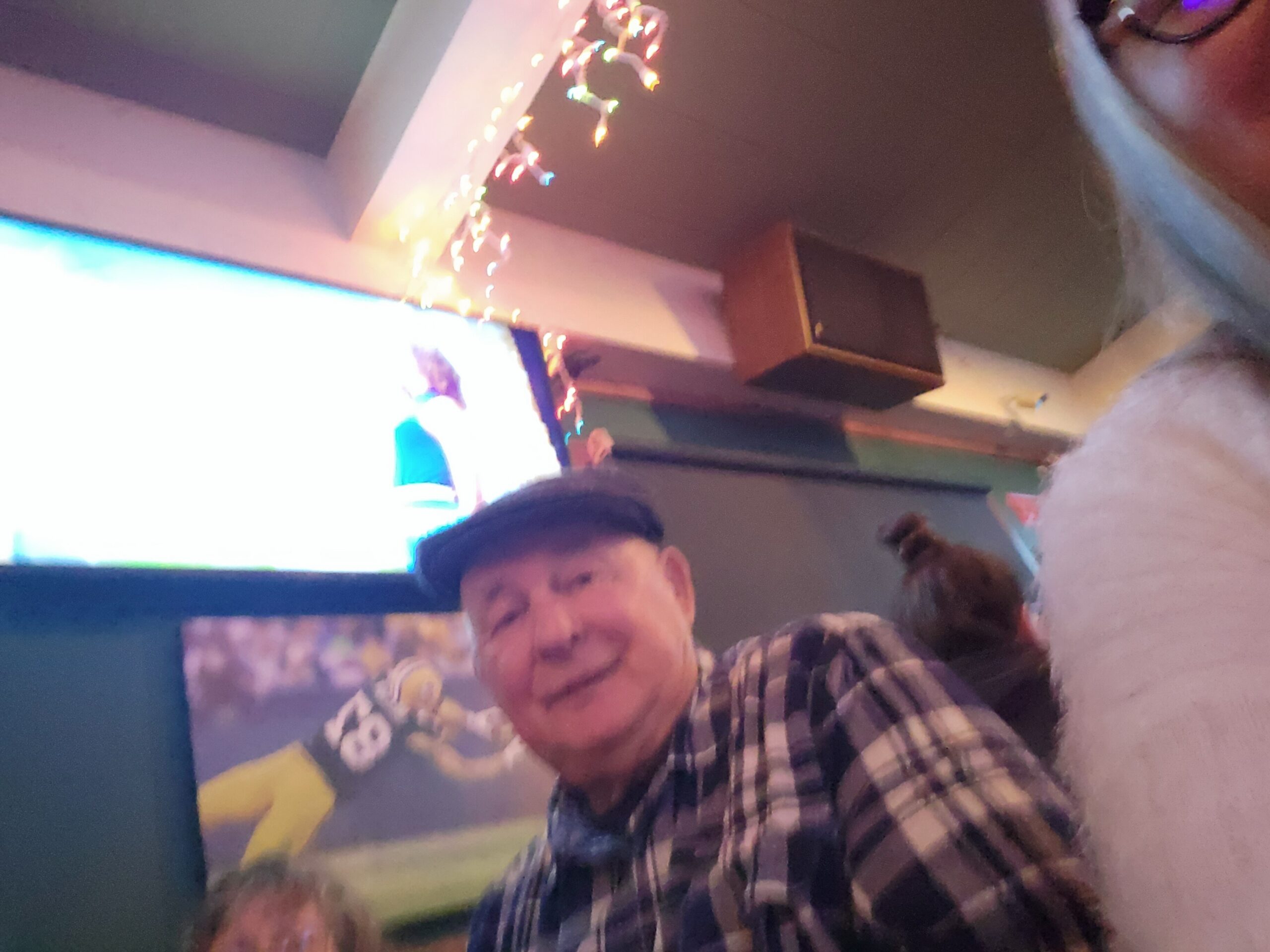 Smiling man in a black-and-white plaid shirt posing at a party, with colorful string lights in the background