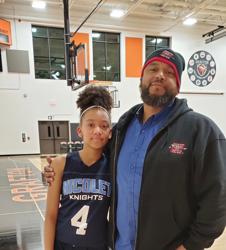 Young girl in Nicollet Knights jersey (number 4) standing with a man in a blue shirt and black jacket in a gymnasium.