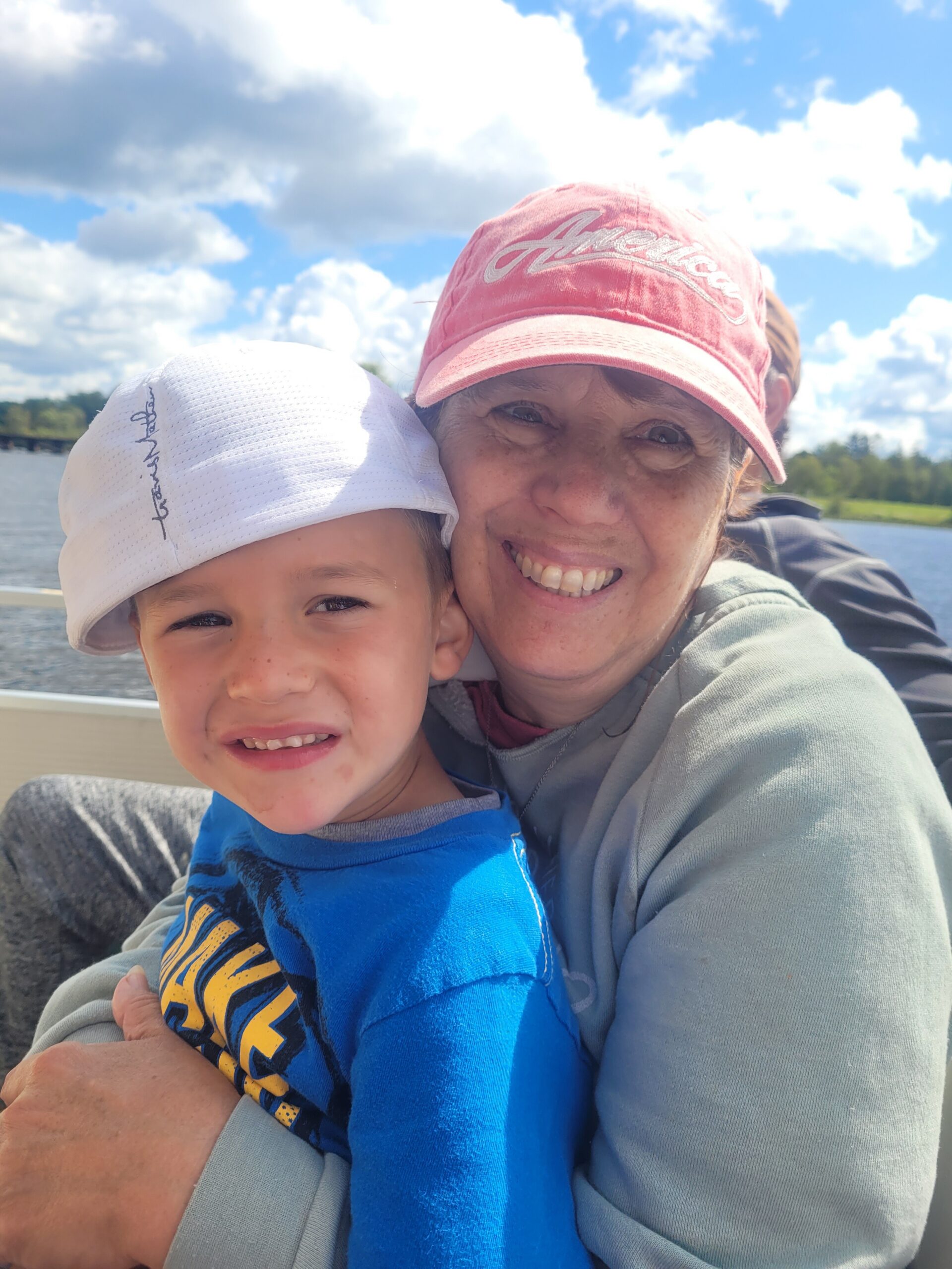 Smiling woman and child posing for a selfie on a boat with a lake and blue sky in the background.