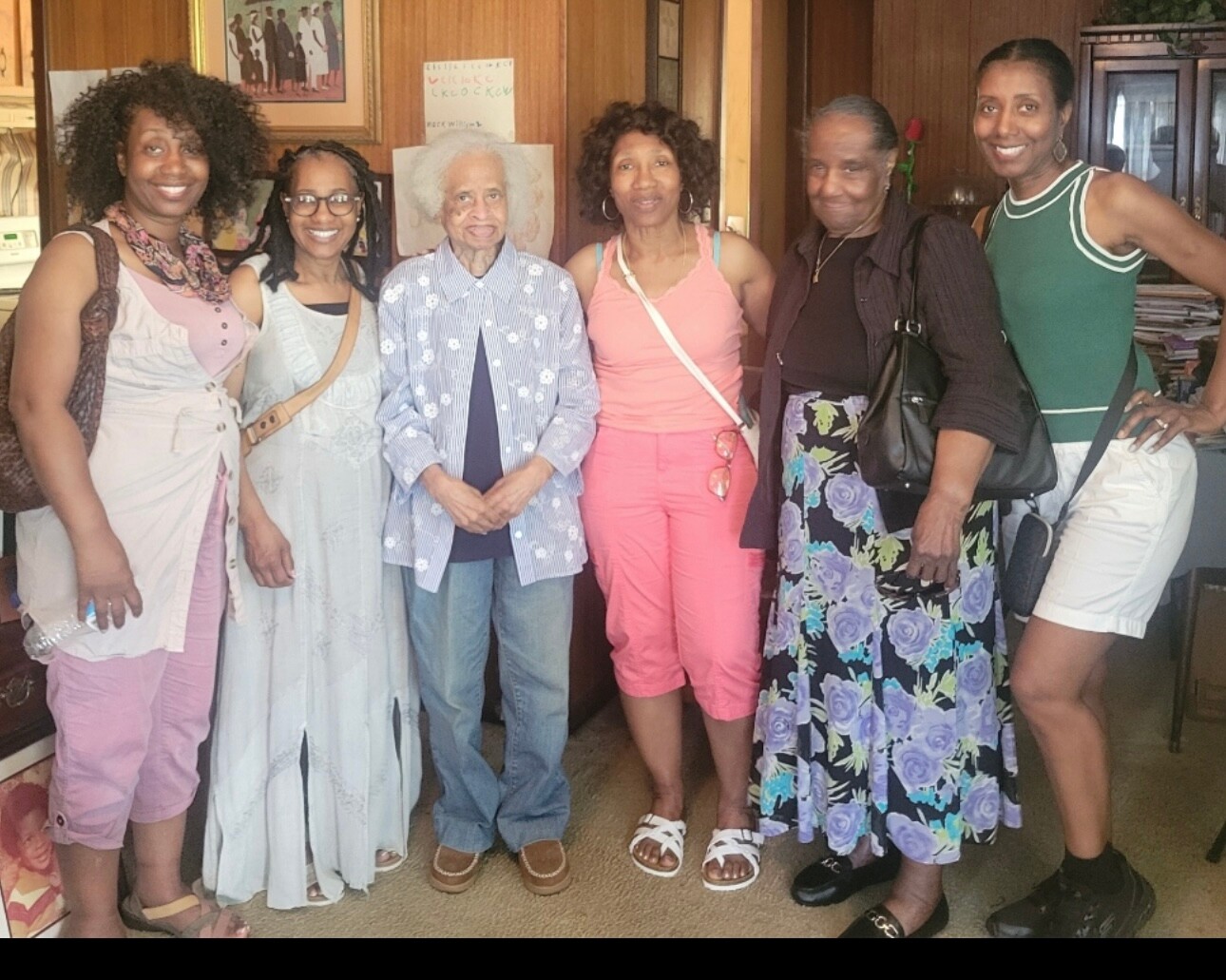 Six women of different ages posing together indoors, smiling for a group photo.