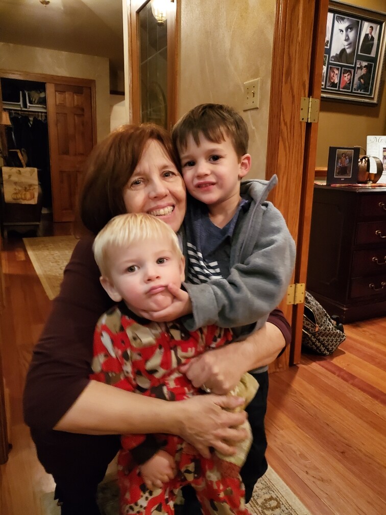 Grandmother smiling as she hugs two young children indoors in a cozy hallway of a home.