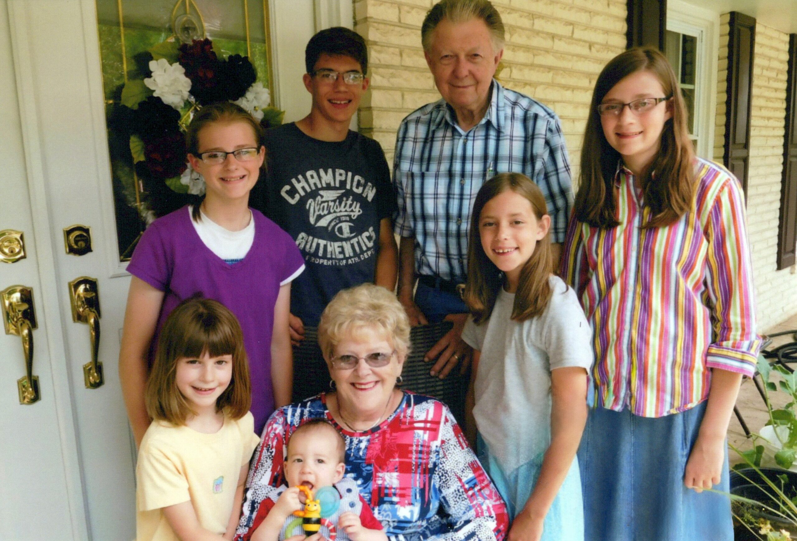 Multigenerational family posing on a front porch in front of a white door and brick wall.