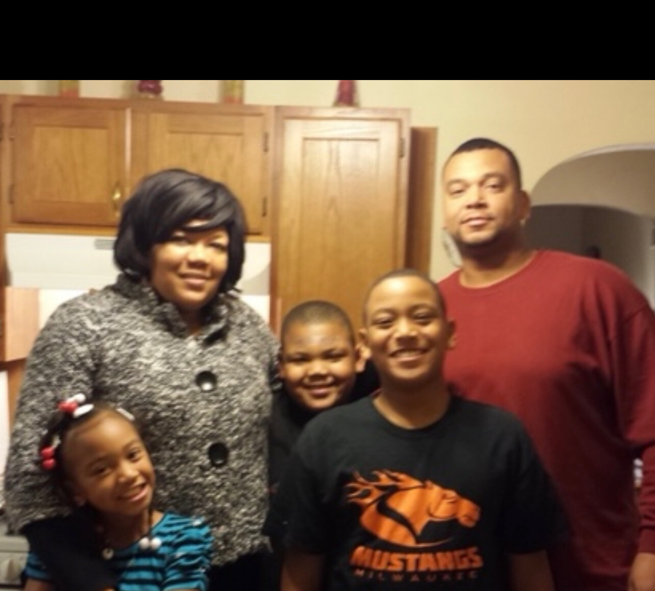Family of five posing in a kitchen, smiling at the camera.
