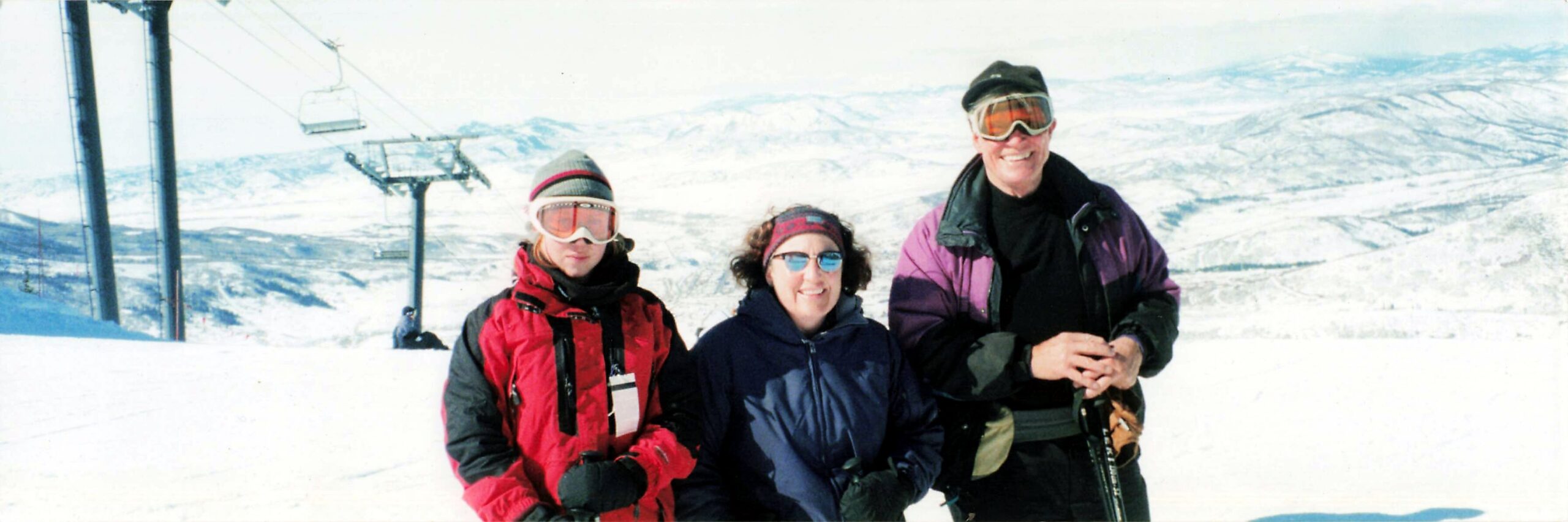 Three skiers posing together on a snowy mountainside with a chairlift in the background.