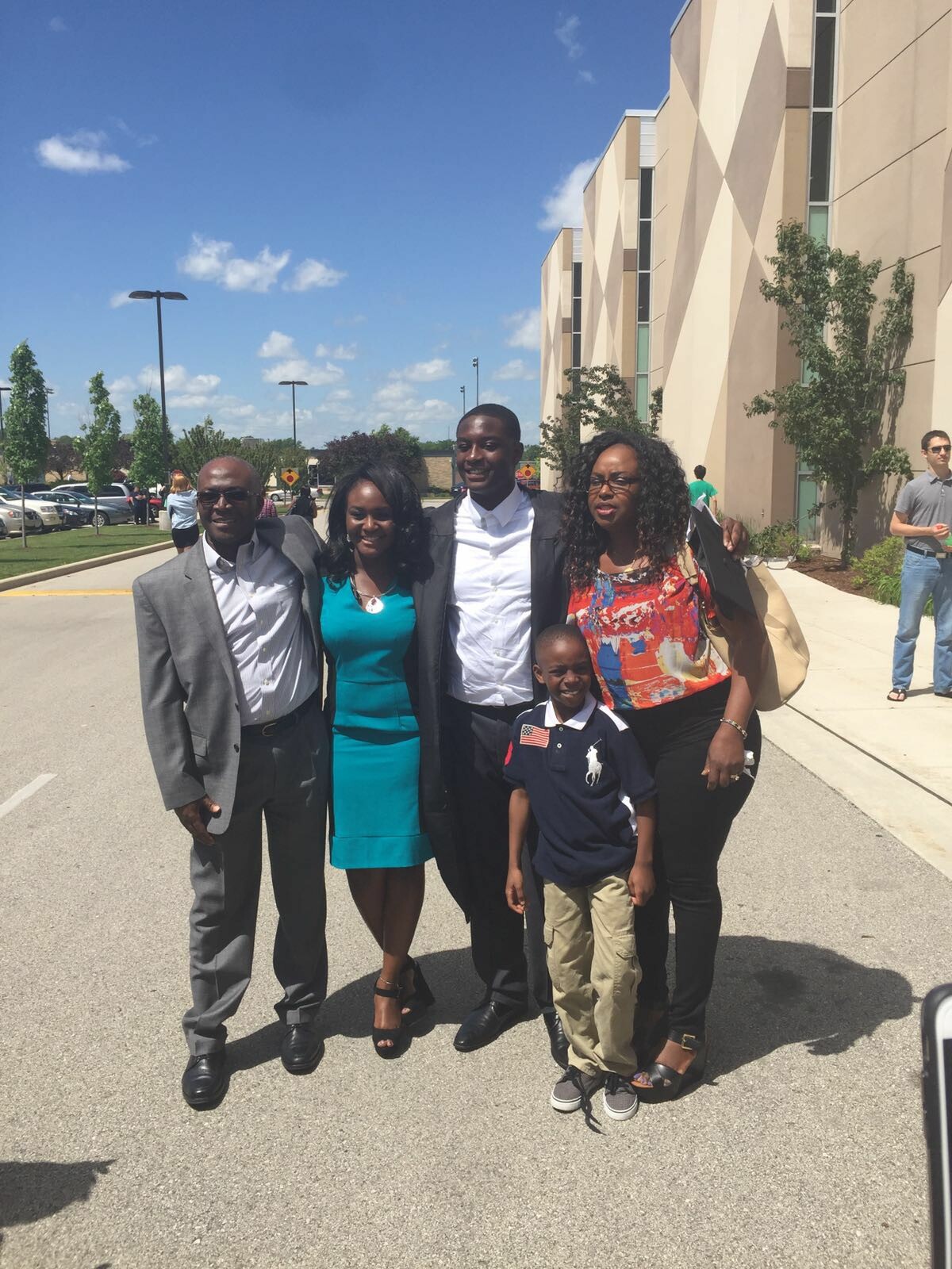 Group of five people posing together outside a modern beige building on a sunny day, smiling at the camera.