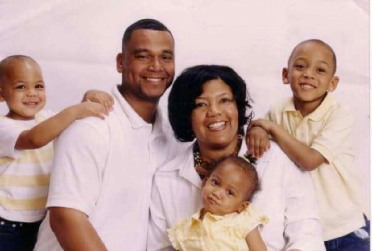 Family portrait: father and mother with three children smiling and posing together in a studio setting.
