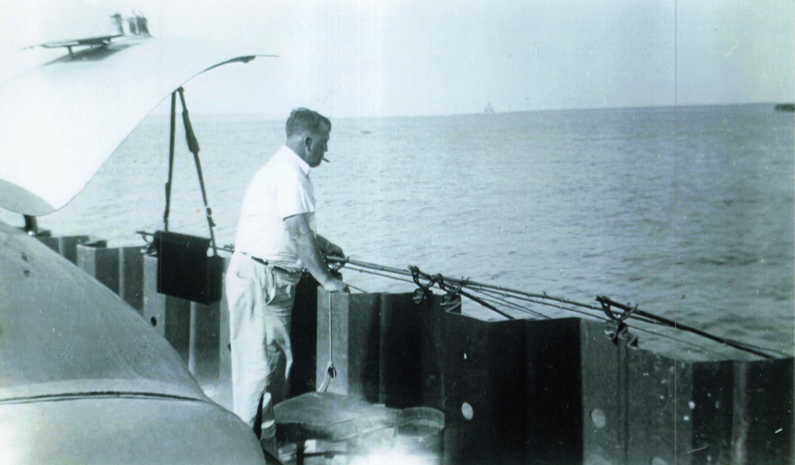 Man wearing a white shirt standing at a ship’s railing, smoking a cigarette and gazing over the ocean.