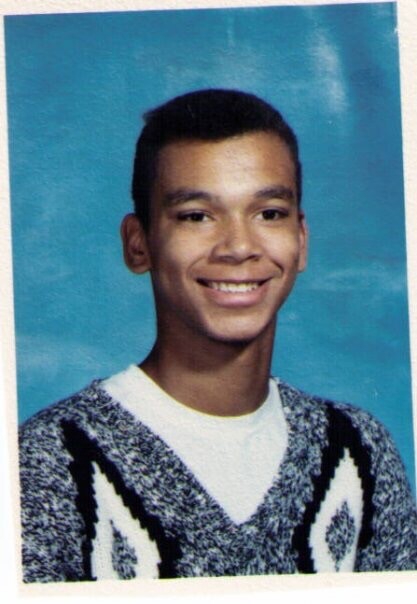 Smiling young man in a patterned knit sweater photographed against a blue backdrop (school portrait).