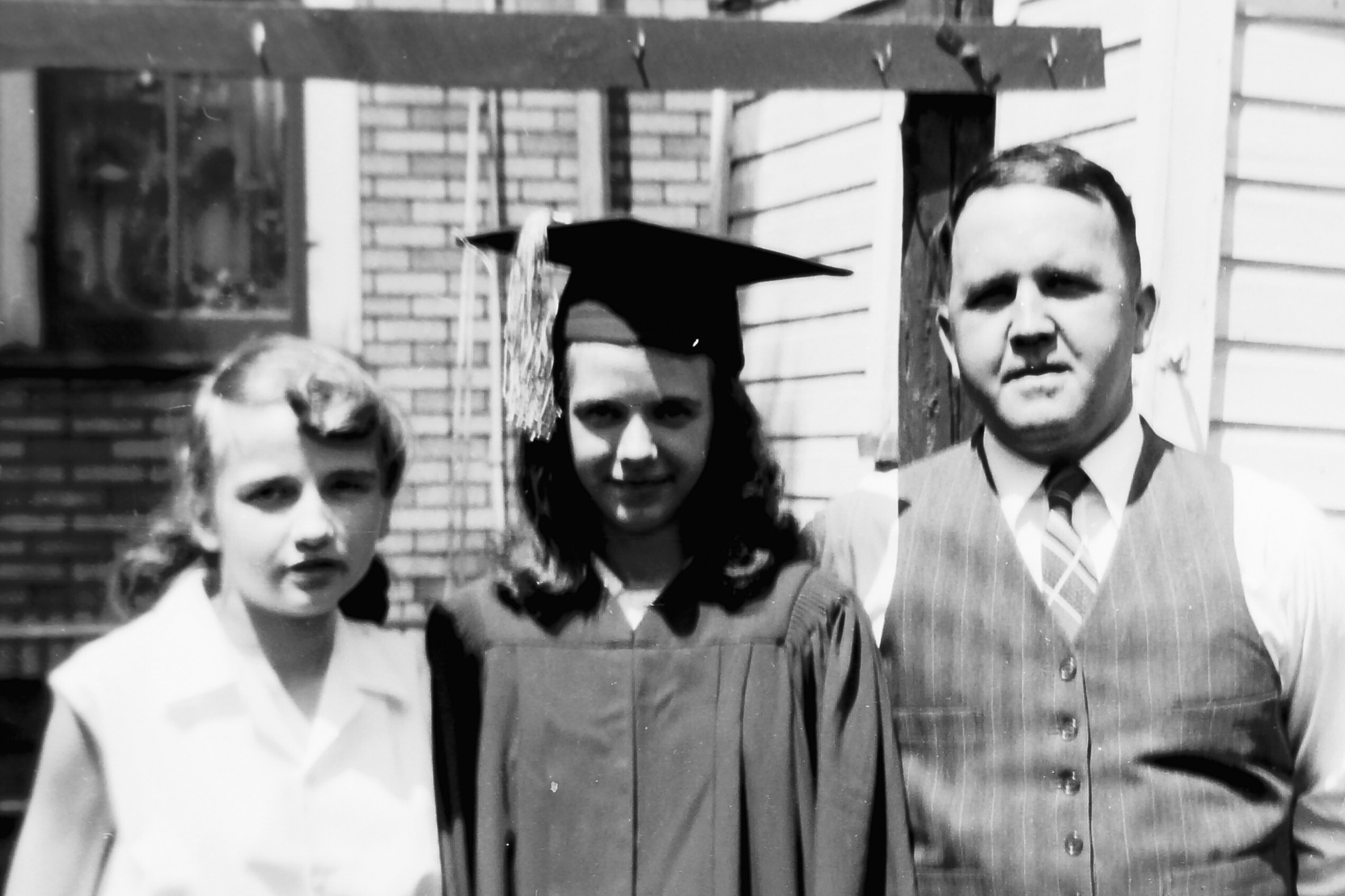 Group of graduates posing outside a house, wearing caps and gowns, smiling for the camera.