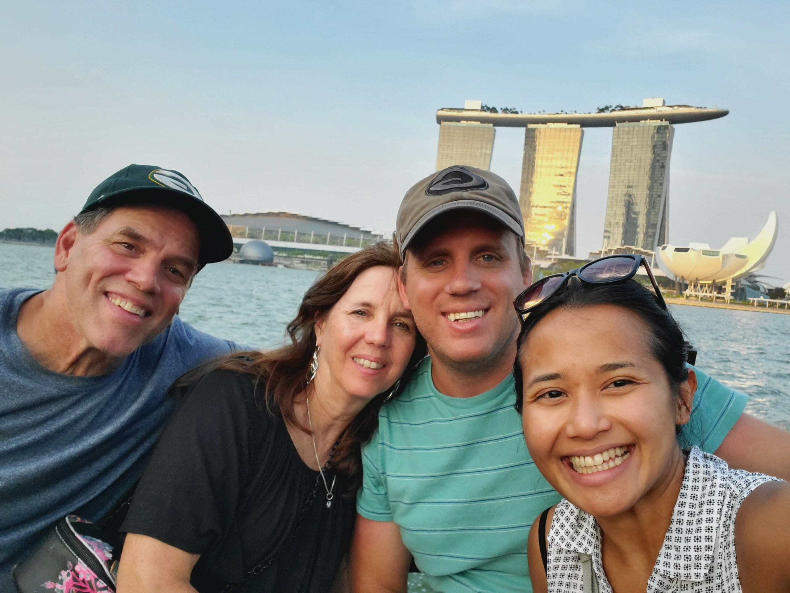 Smiling group of friends taking a selfie by the water with Marina Bay Sands hotel in Singapore in the background.