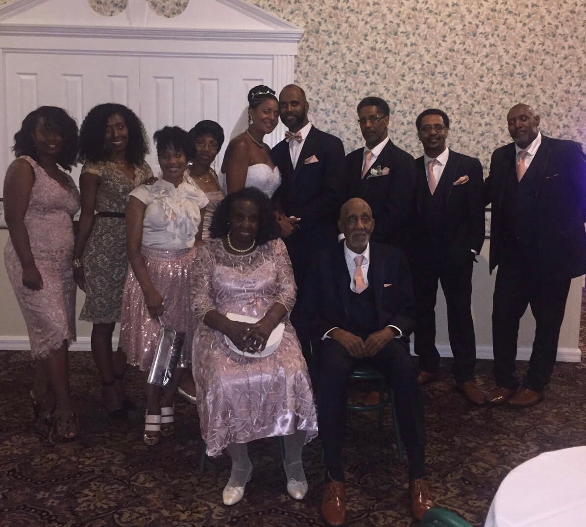 Bride and groom pose with family at a formal wedding reception, everyone dressed in elegant attire.