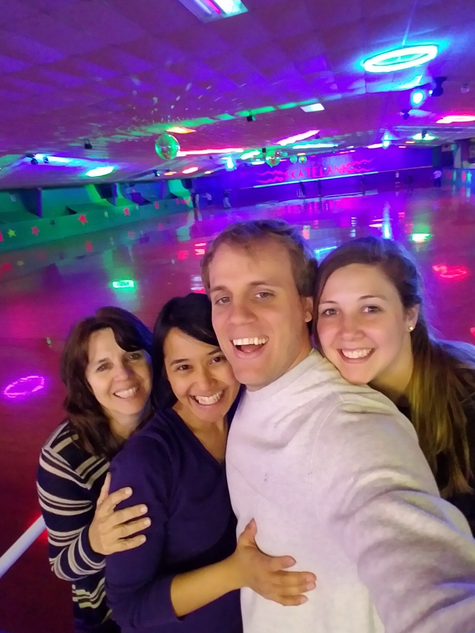 Group of four friends taking a selfie in a colorful, neon-lit roller skating rink, smiling and embracing each other.