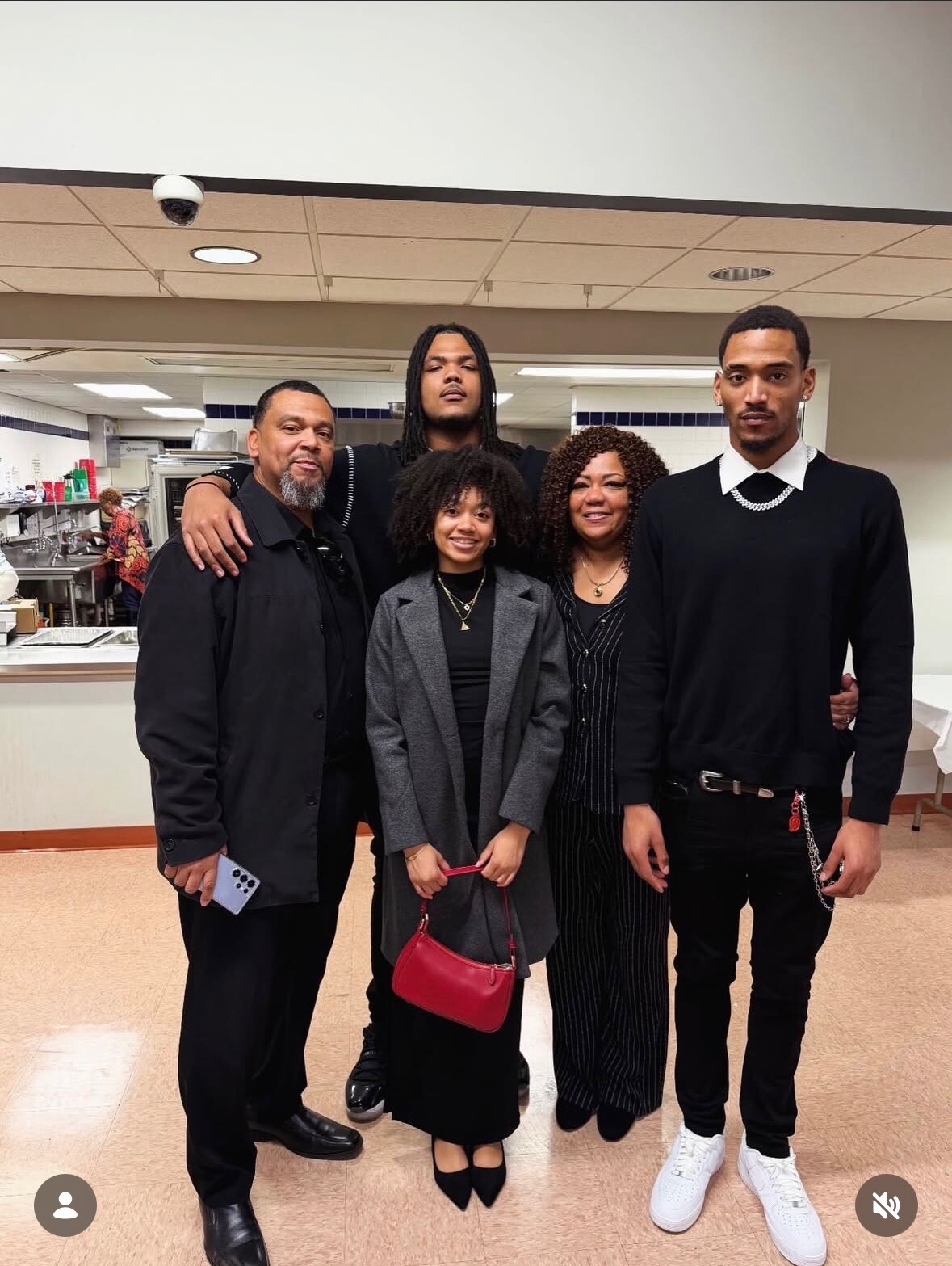 Five people stand together indoors in a cafeteria, posing for a group photo and smiling at the camera.