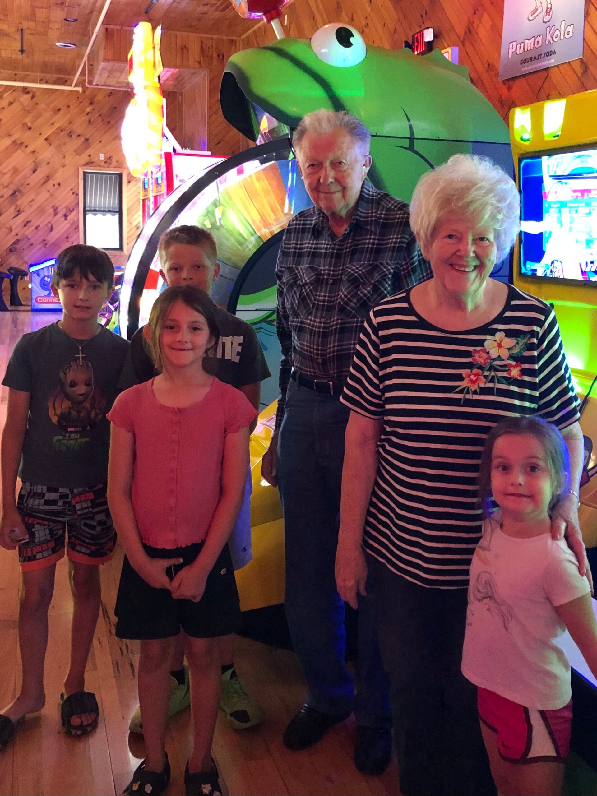 Group of six posing in an arcade, with a large green frog prop behind them.