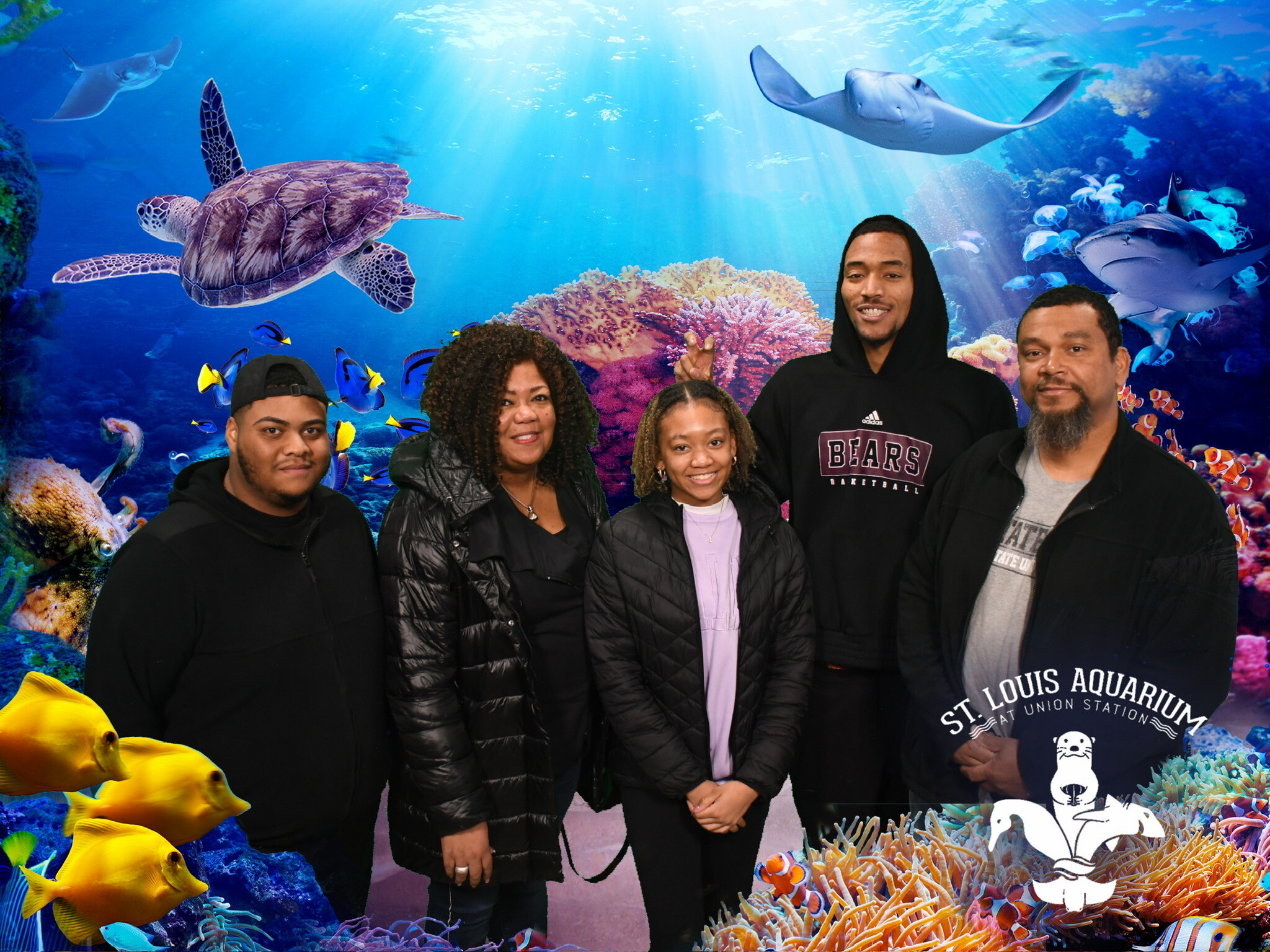 Group of five people posing in front of a colorful aquarium backdrop with fish and coral reefs behind them.