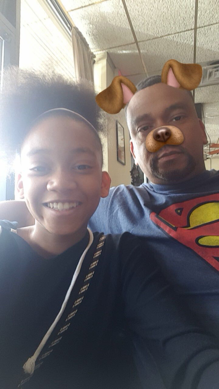 Boy and man posing for a selfie indoors; the man wears a dog filter with ears and nose over his face