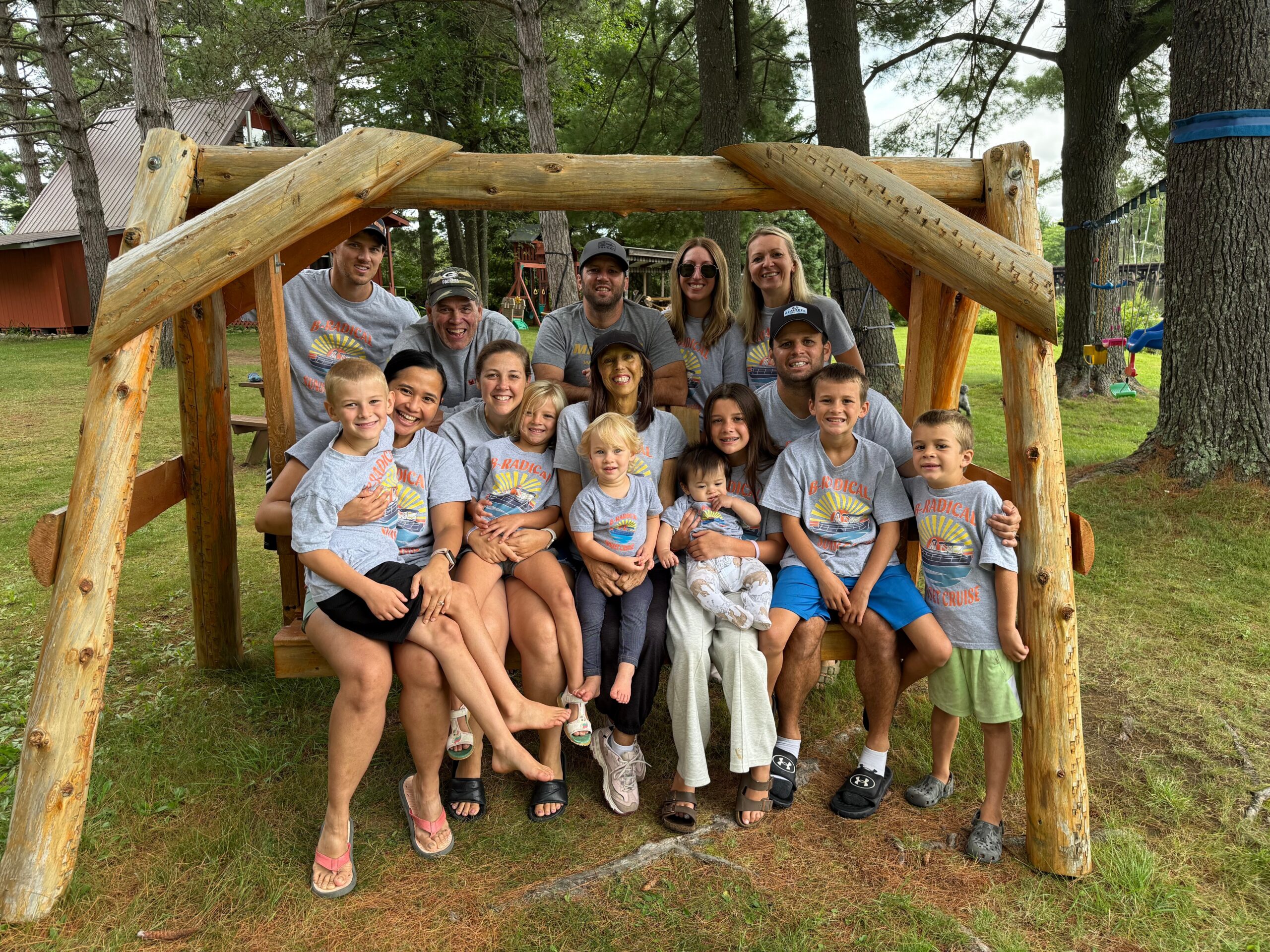 Group of smiling adults and children posing inside a large wooden play structure in a park.